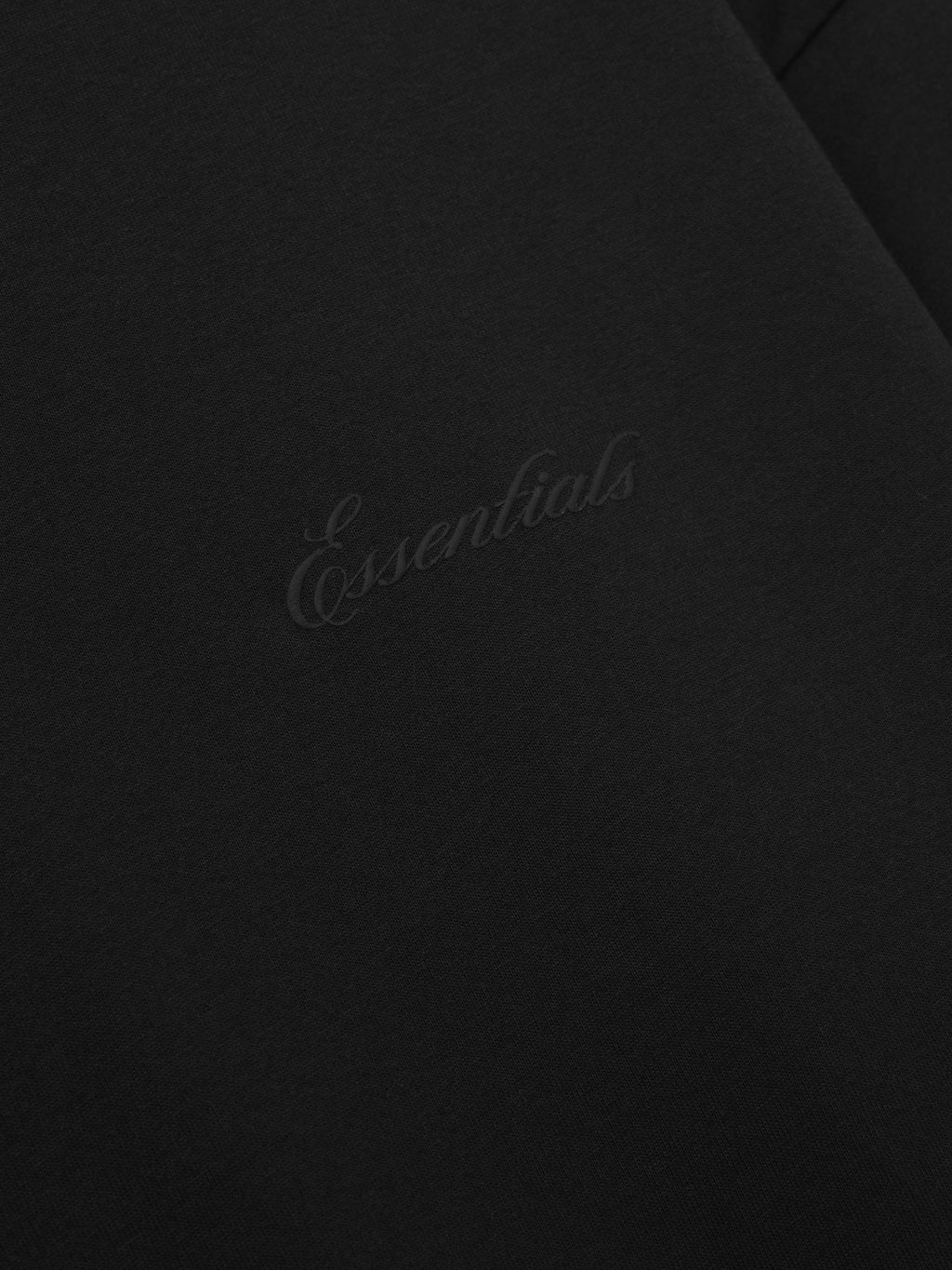 close-up of black cotton jersey fabric featuring subtle embossed Essentials script logo on front