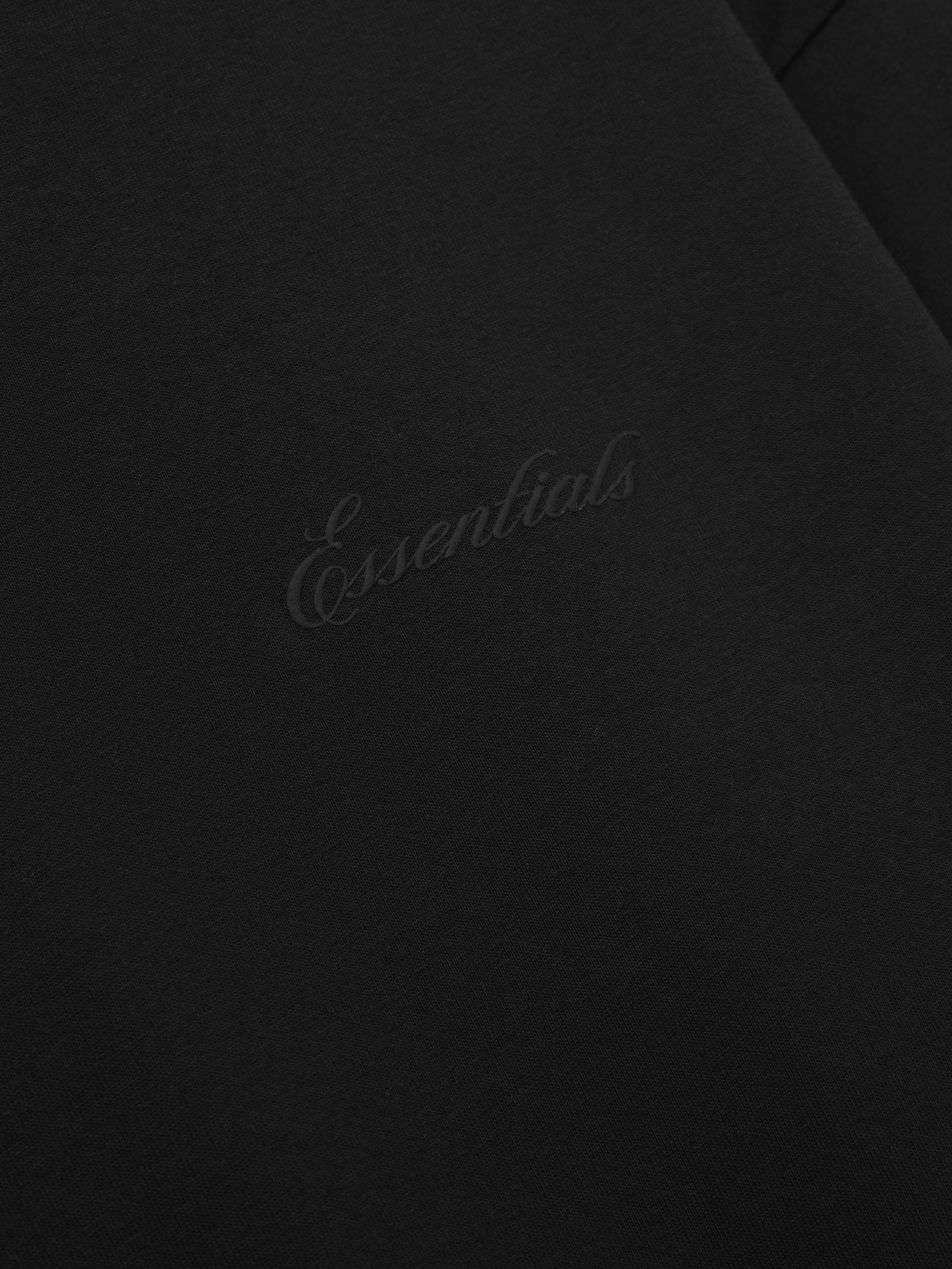close-up of black cotton jersey fabric featuring subtle embossed Essentials script logo on front