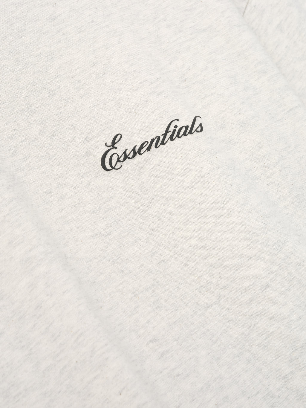 off-white cotton jersey fabric close-up with black Essentials script logo on chest of long sleeve tee