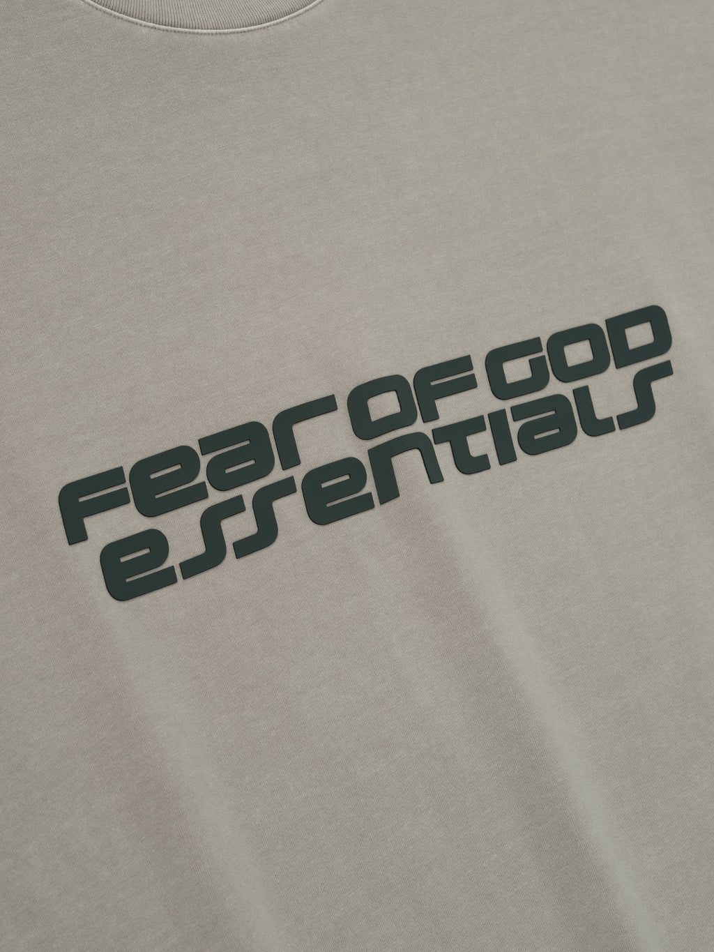 Close-up of smoke grey Fear of God Essentials 90s Tee showing bold black slanted logo text on soft cotton fabric front
