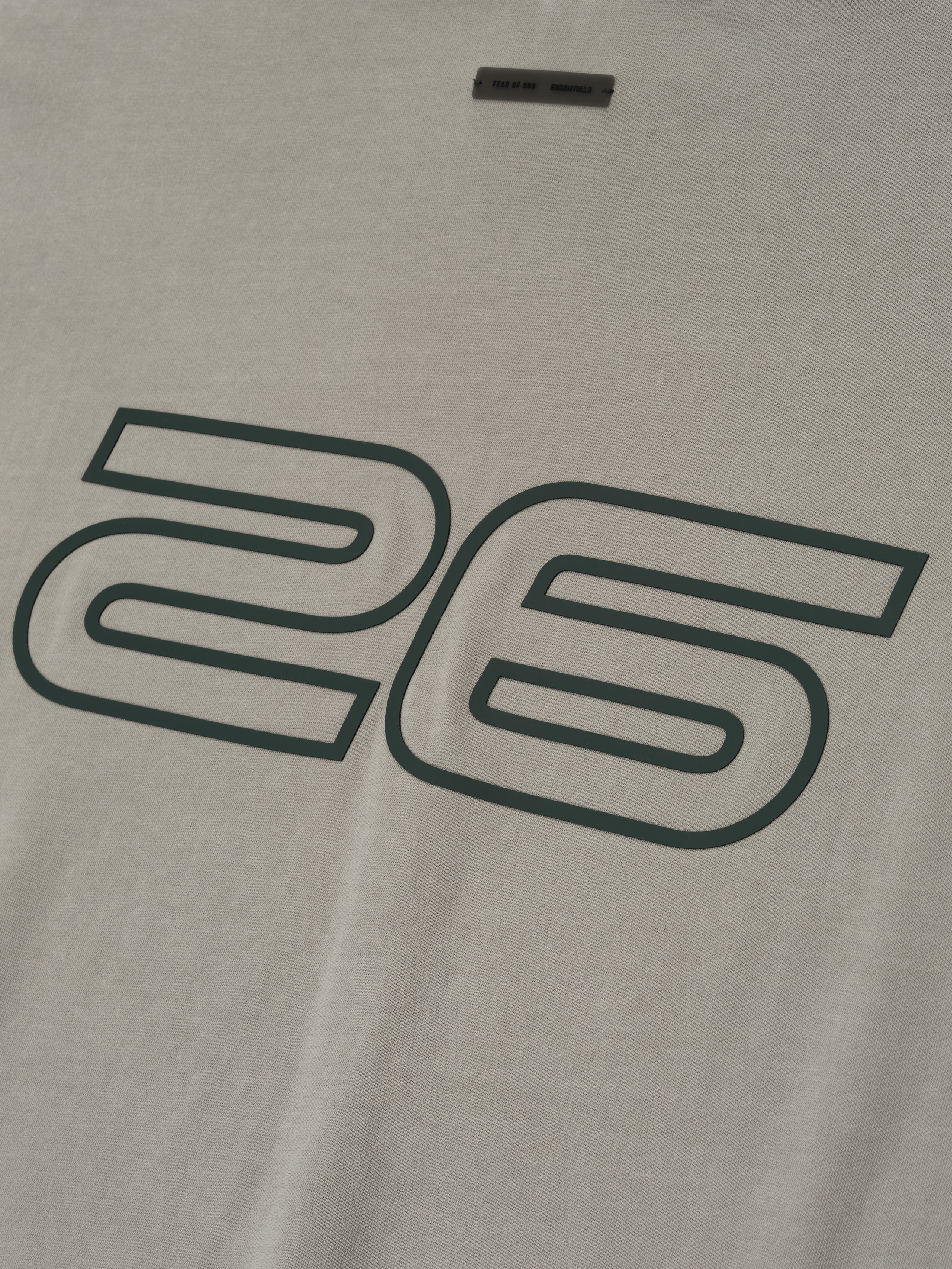Close-up of smoke grey Fear of God Essentials 90s Tee showing large outlined 26 print on soft cotton fabric