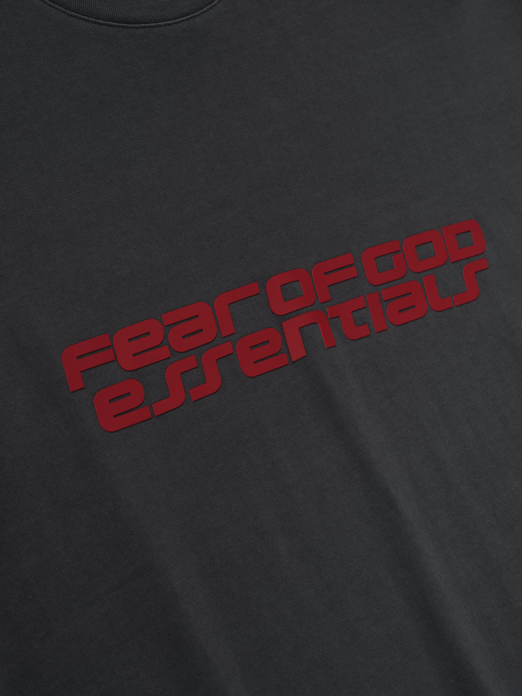 Close-up of iron grey Fear of God Essentials 90s Tee showing bold red logo text on smooth soft fabric front, gallery first image