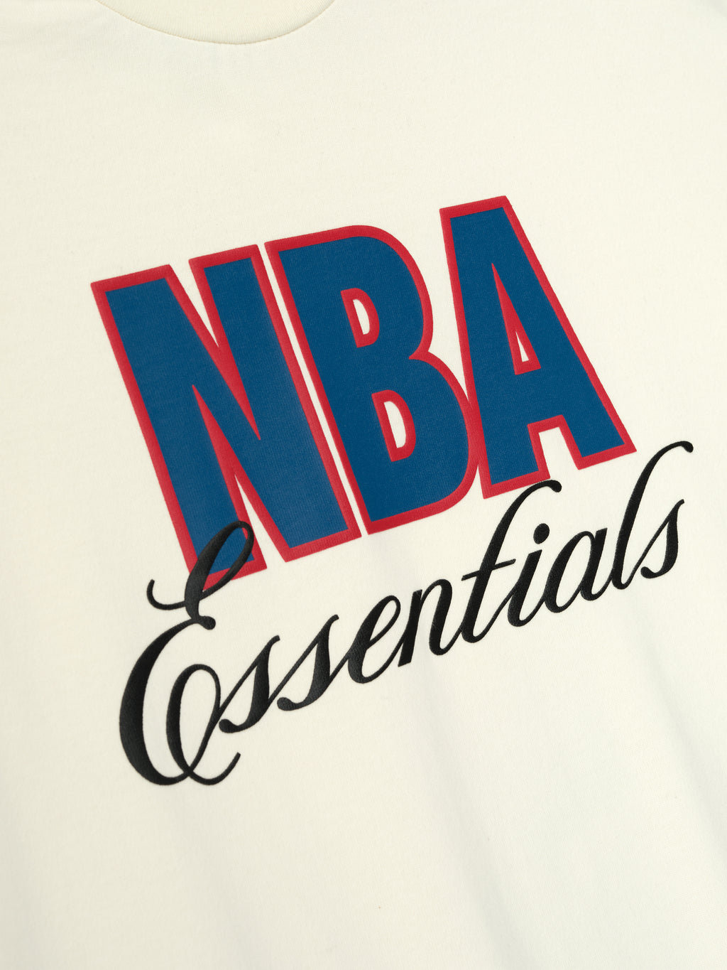 Close-up of cream white NBA 90s Tee with bold blue and red NBA lettering and black Essentials script on soft fabric