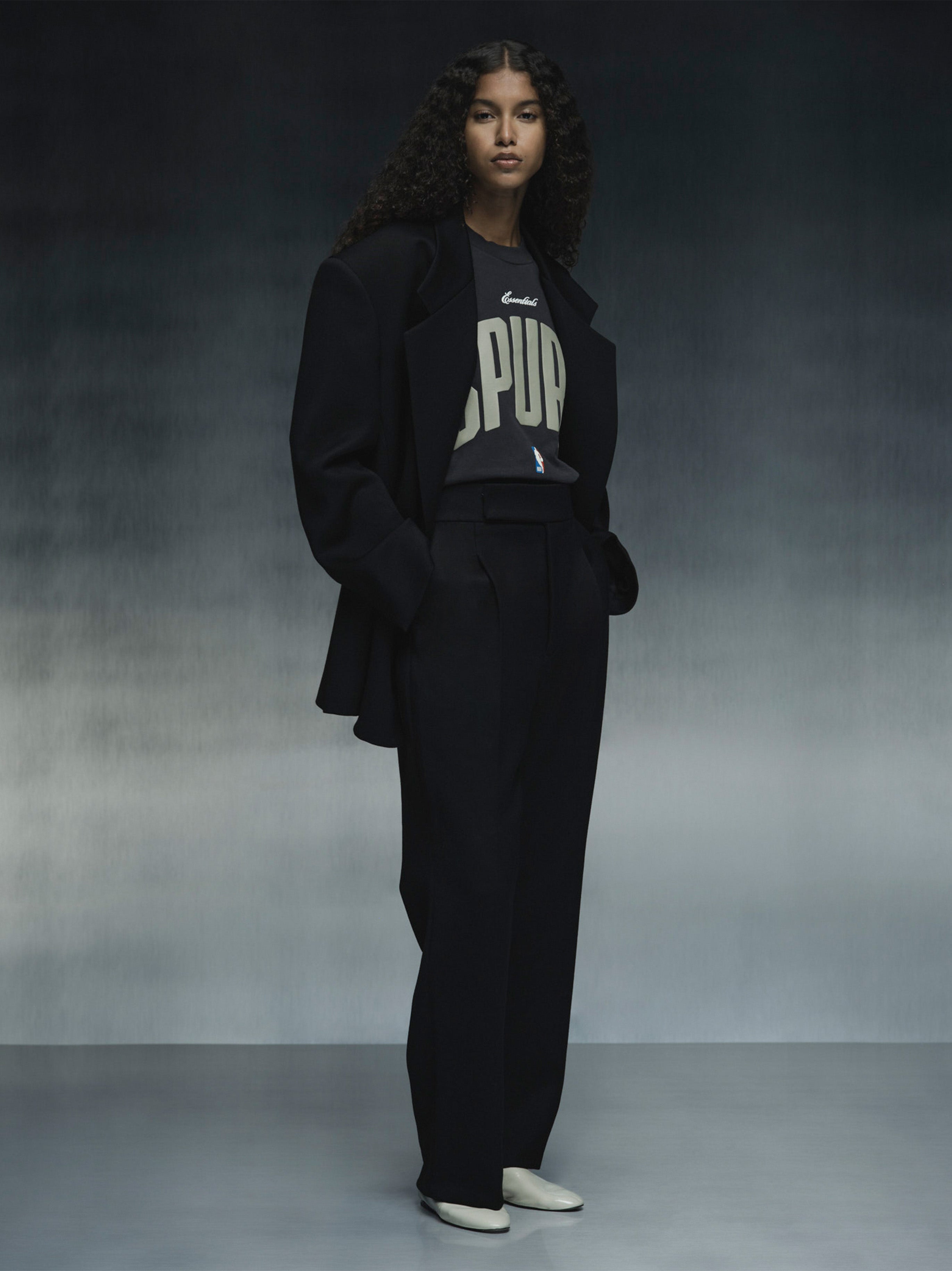 Full-length shot of model wearing black Spurs 90s Tee under oversized black blazer with wide-leg trousers, gallery 0 file 125NB252231F_Black.jpg