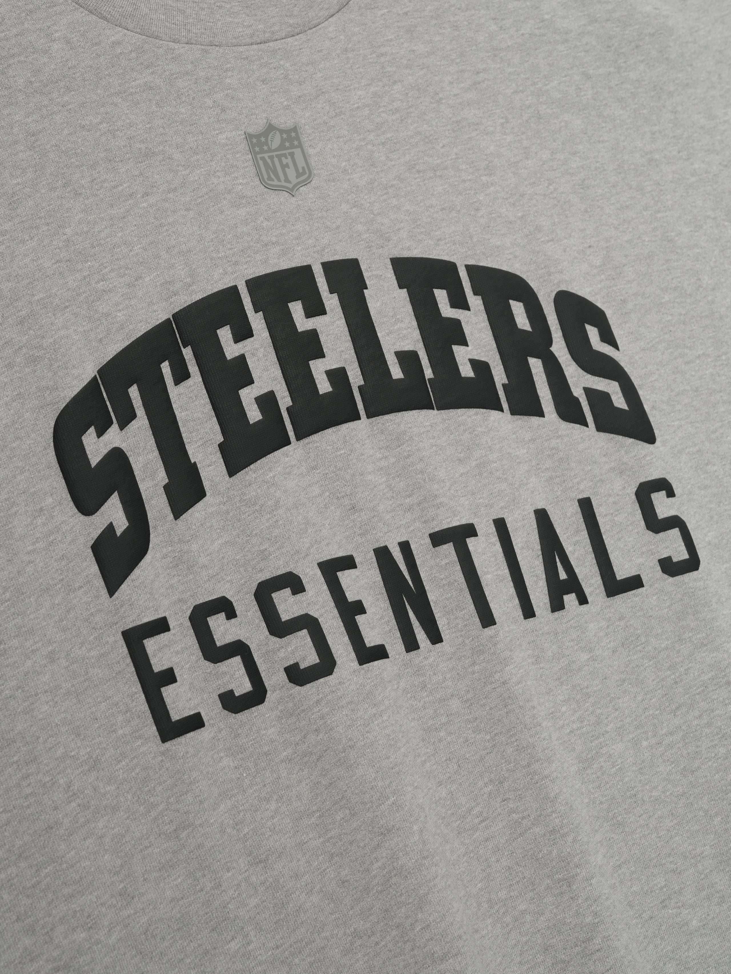 Close-up of concrete heather Steelers 90s 3/4 Sleeve Football Tee showing curved black Steelers text and Essentials below chest