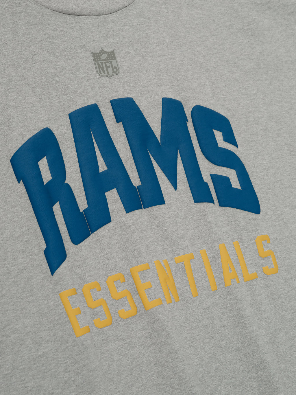 Close-up of concrete heather Rams 90s 3/4 Sleeve Football Tee showing blue Rams text and gold Essentials below center chest with subtle NFL logo above