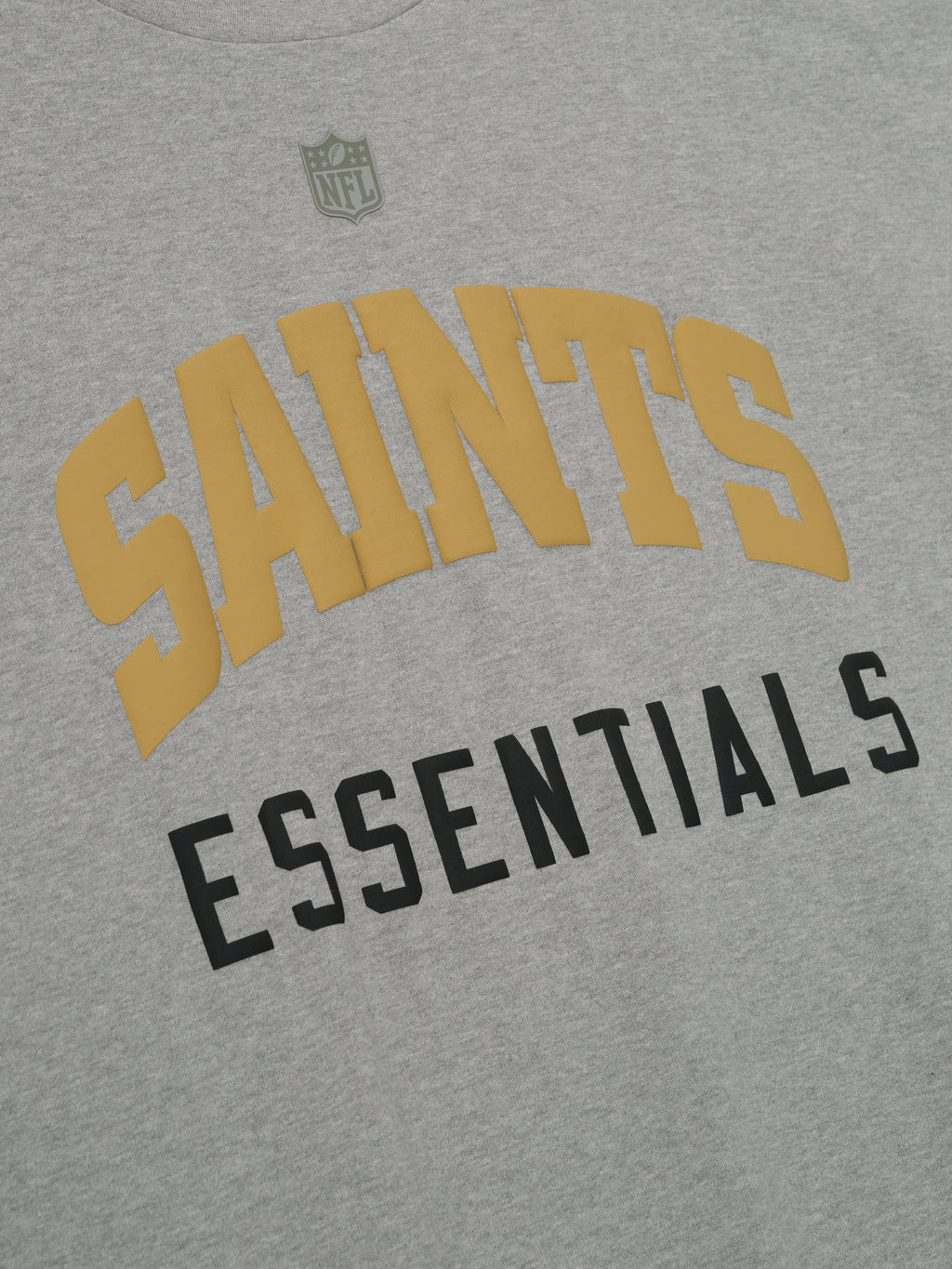 Close-up of concrete heather Saints 90s 3/4 Sleeve Football Tee showing gold Saints arched text and black Essentials below center chest