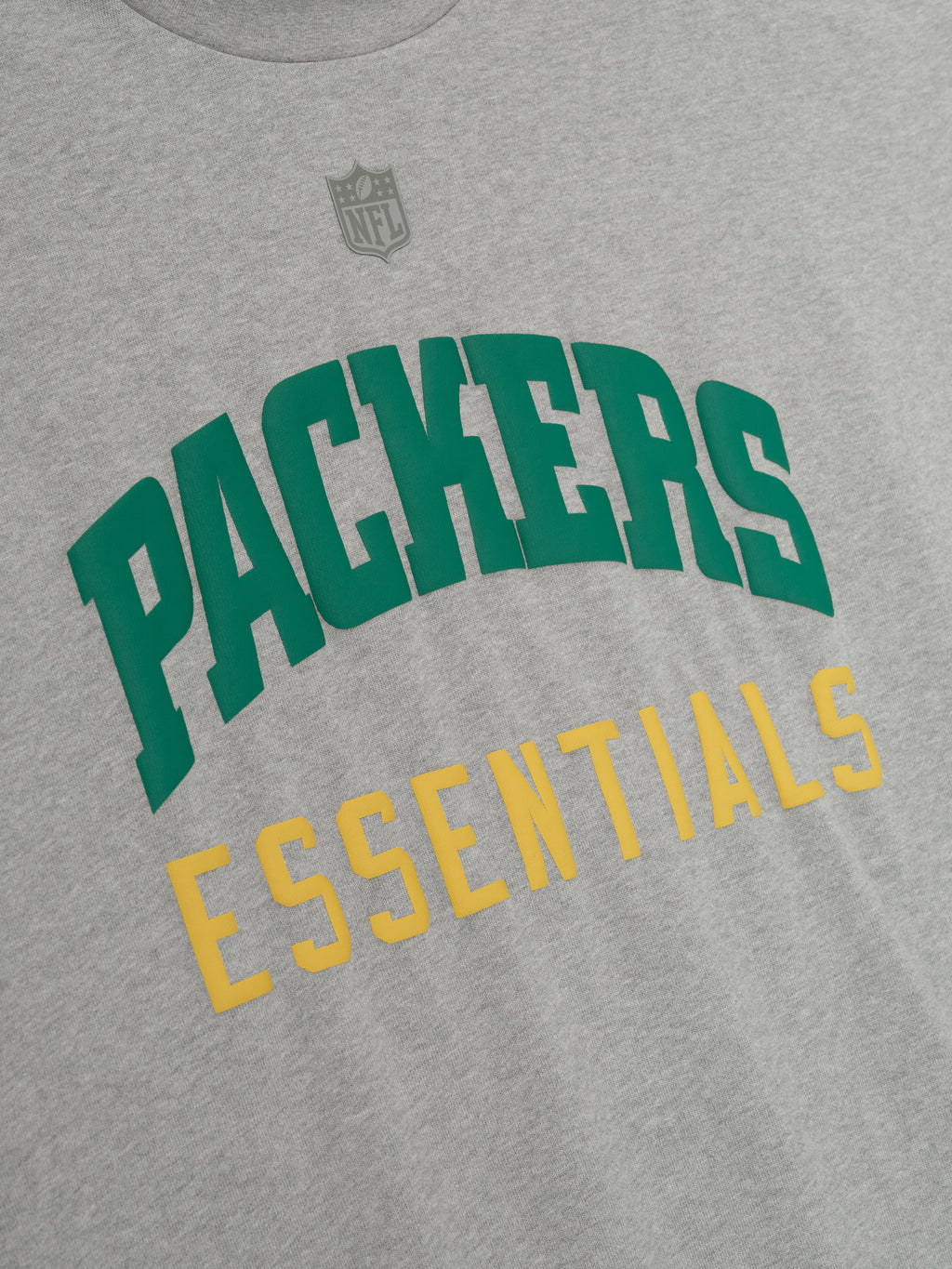 Close-up of concrete heather Packers 90s 3/4 Sleeve Football Tee showing green PACKERS and yellow ESSENTIALS text on chest