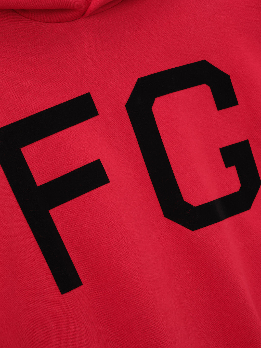close-up of red hoodie front with large black felt "FG" lettering printed on smooth fleece fabric