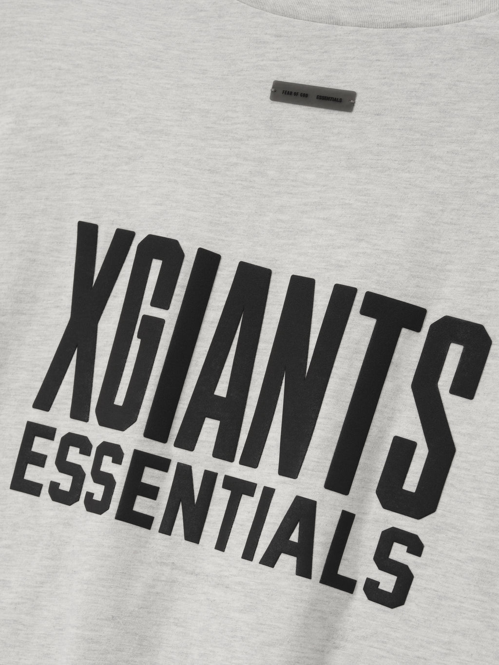 close-up of light gray cotton tee with bold black "XGIANTS ESSENTIALS" text printed on front center
