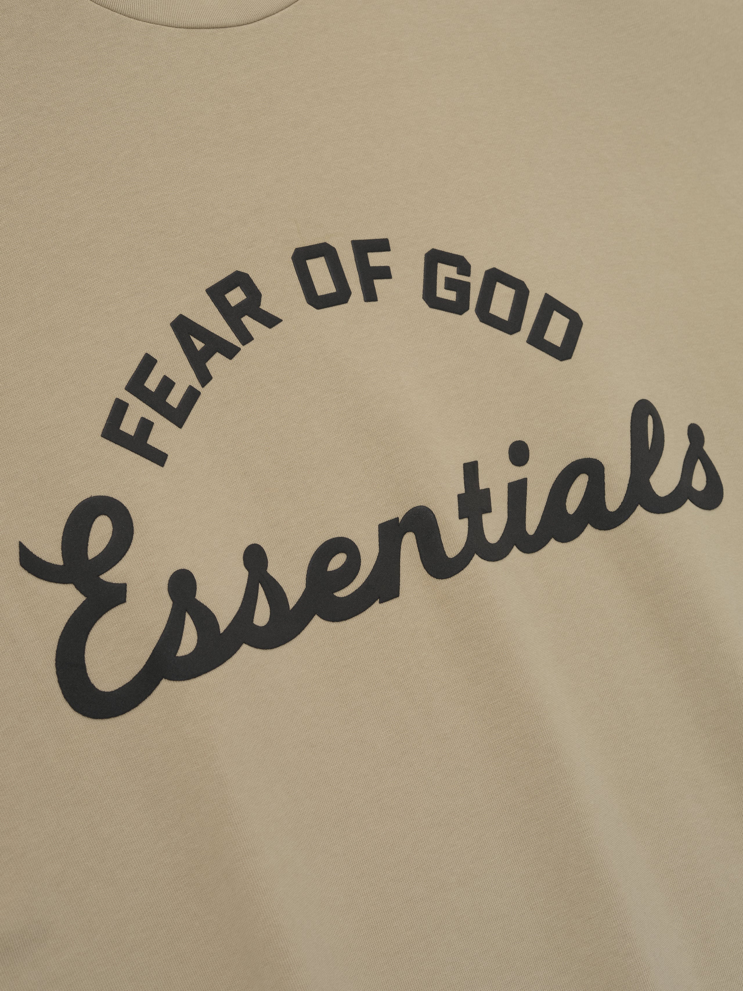 close-up of beige heavyweight cotton tee with arched Fear of God Essentials logo in black print front view