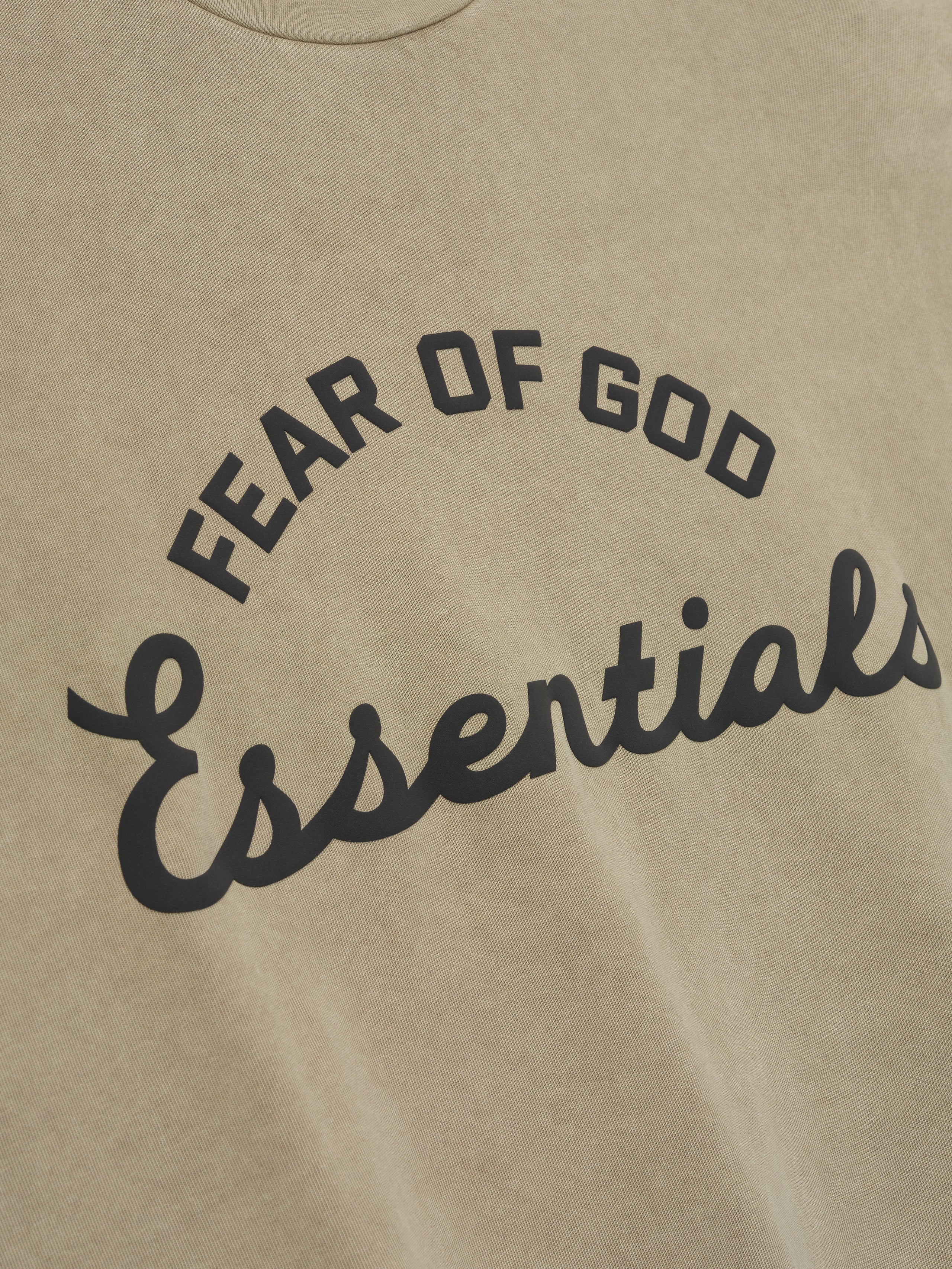 close-up of pigment-dyed vintage beige cotton tee with arched Fear of God Essentials logo in contrasting black print