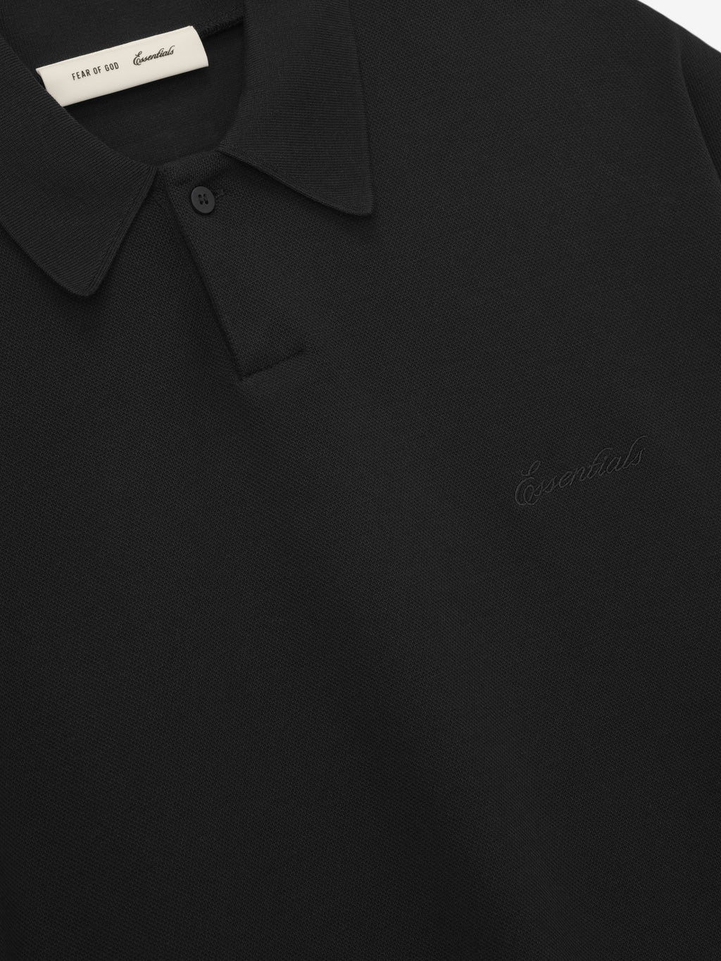 close-up of black medium-weight cotton poly pique polo with classic collar and subtle embossed Essentials branding on chest
