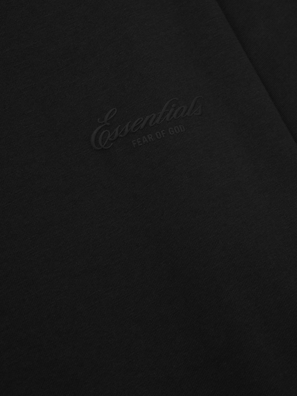 close-up of black cotton jersey fabric with subtle tonal puff-printed Essentials Fear of God logo on long sleeve tee