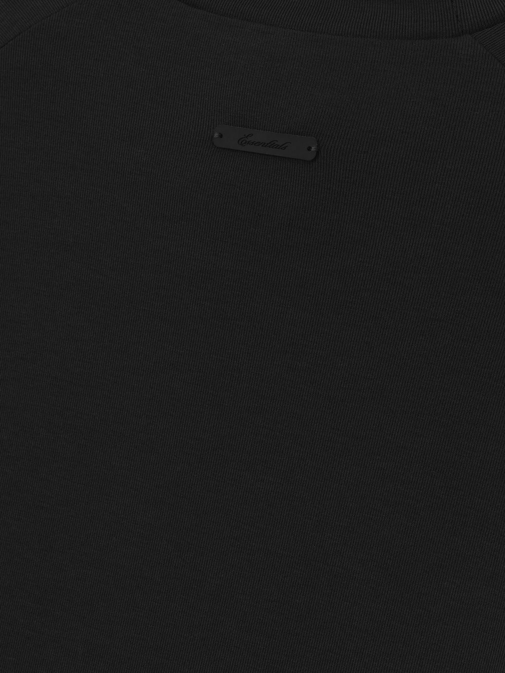 close-up of black ribbed knit fabric with small rectangular black brand label sewn near neckline