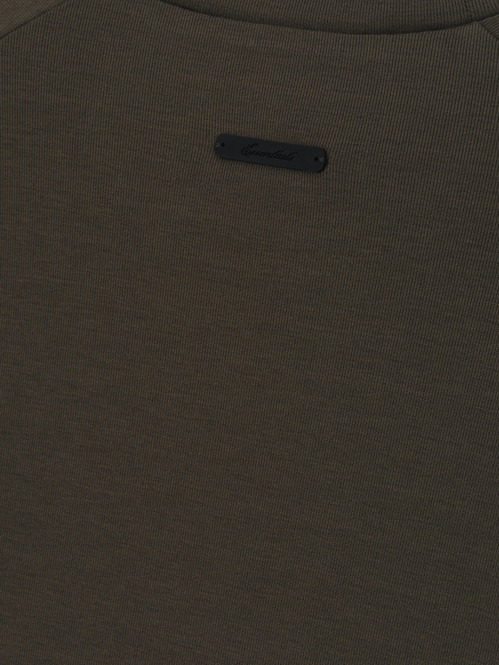close-up of dark olive ribbed knit fabric with small black Essentials logo patch sewn near neckline