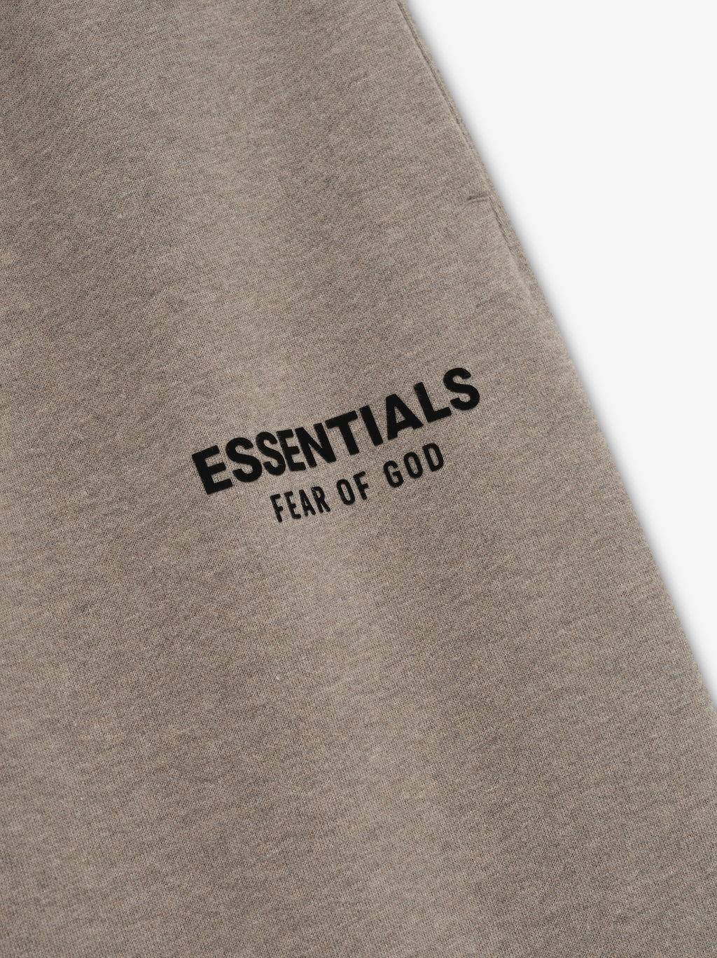Taupe classic sweatpant fabric close-up with black "ESSENTIALS FEAR OF GOD" logo printed on upper thigh area
