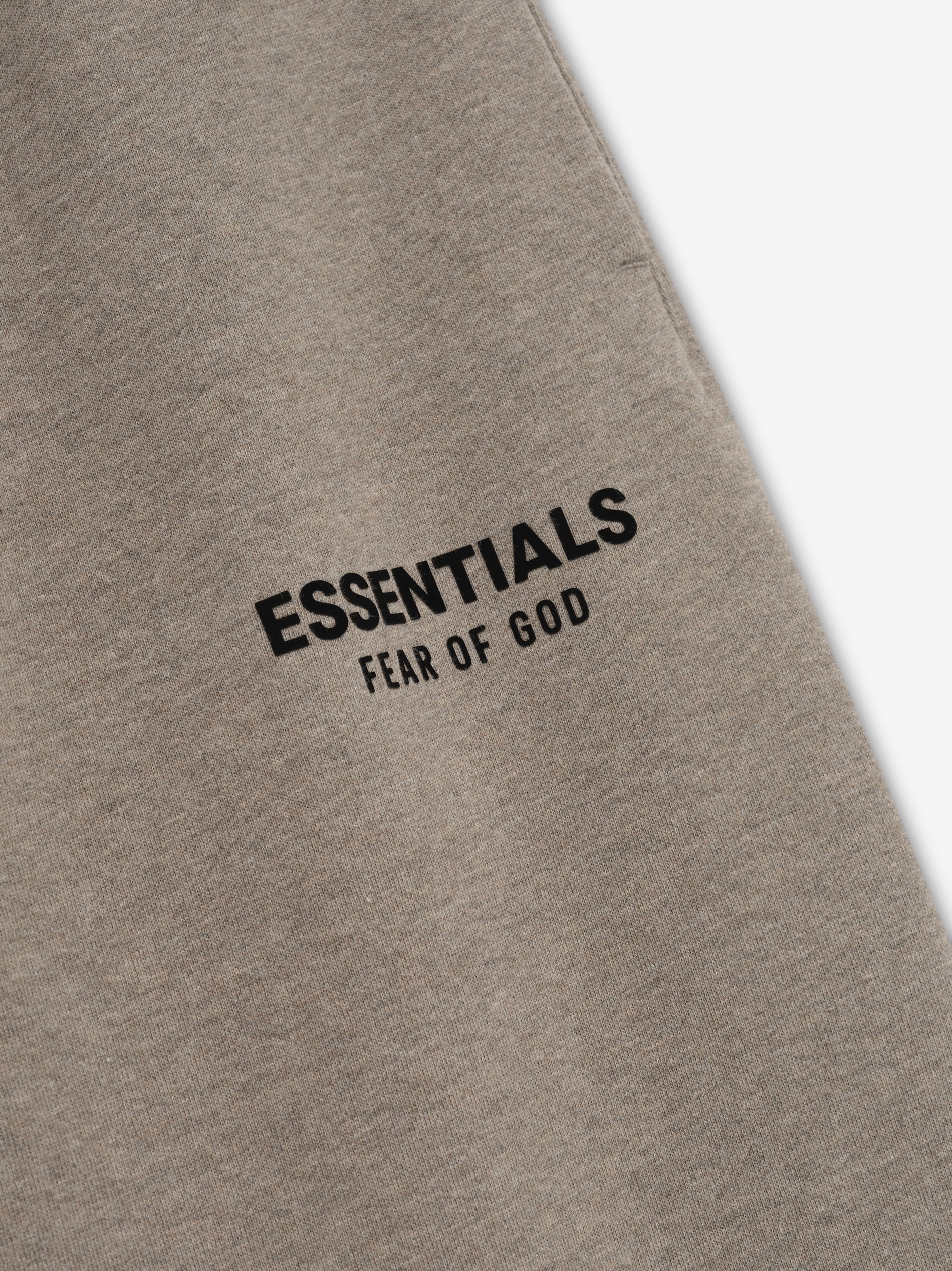 Taupe classic sweatpant fabric close-up with black "ESSENTIALS FEAR OF GOD" logo printed on upper thigh area