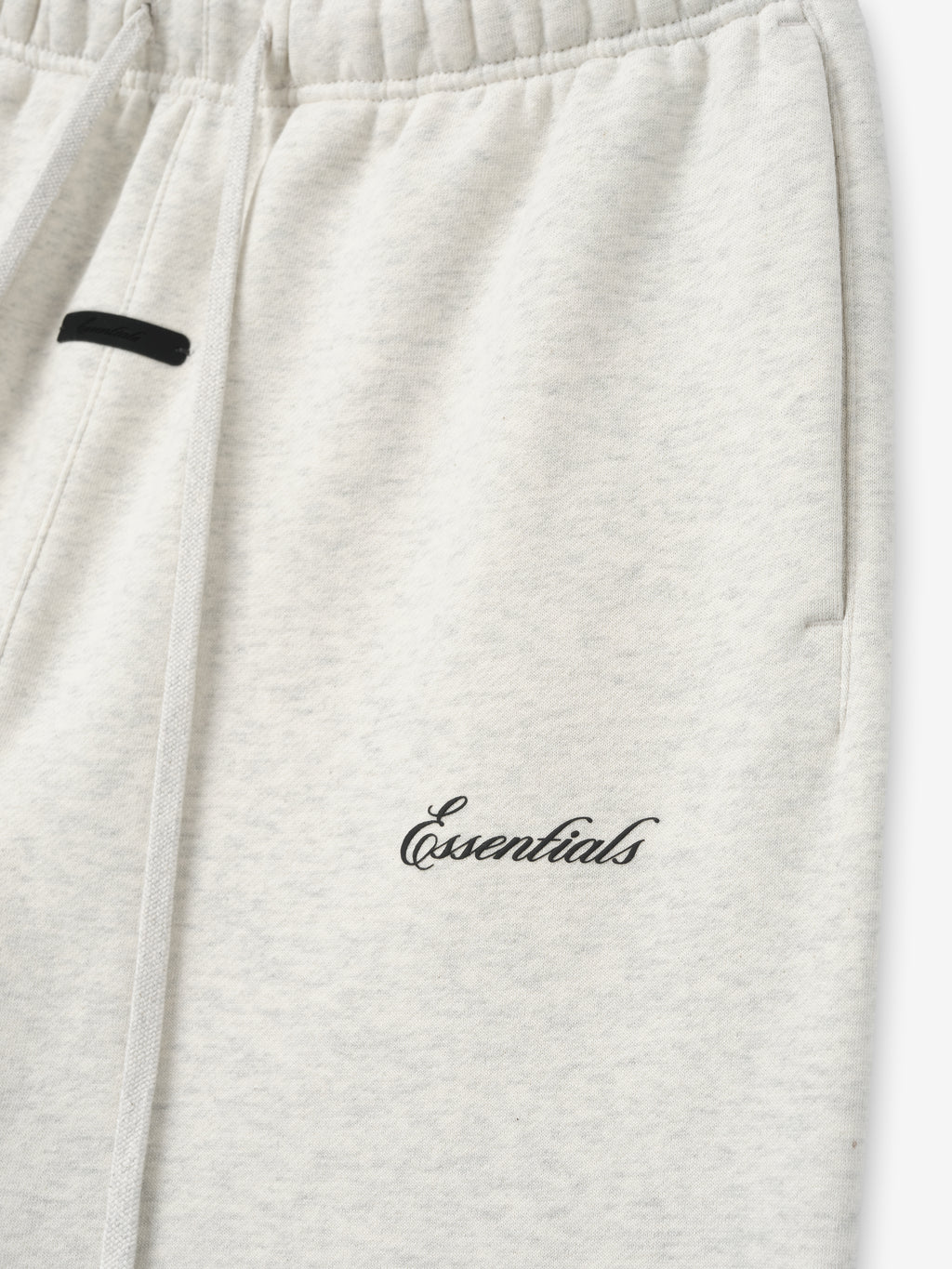 close-up of light heather gray sweatpant with elastic waistband and black puff-printed Essentials logo on thigh