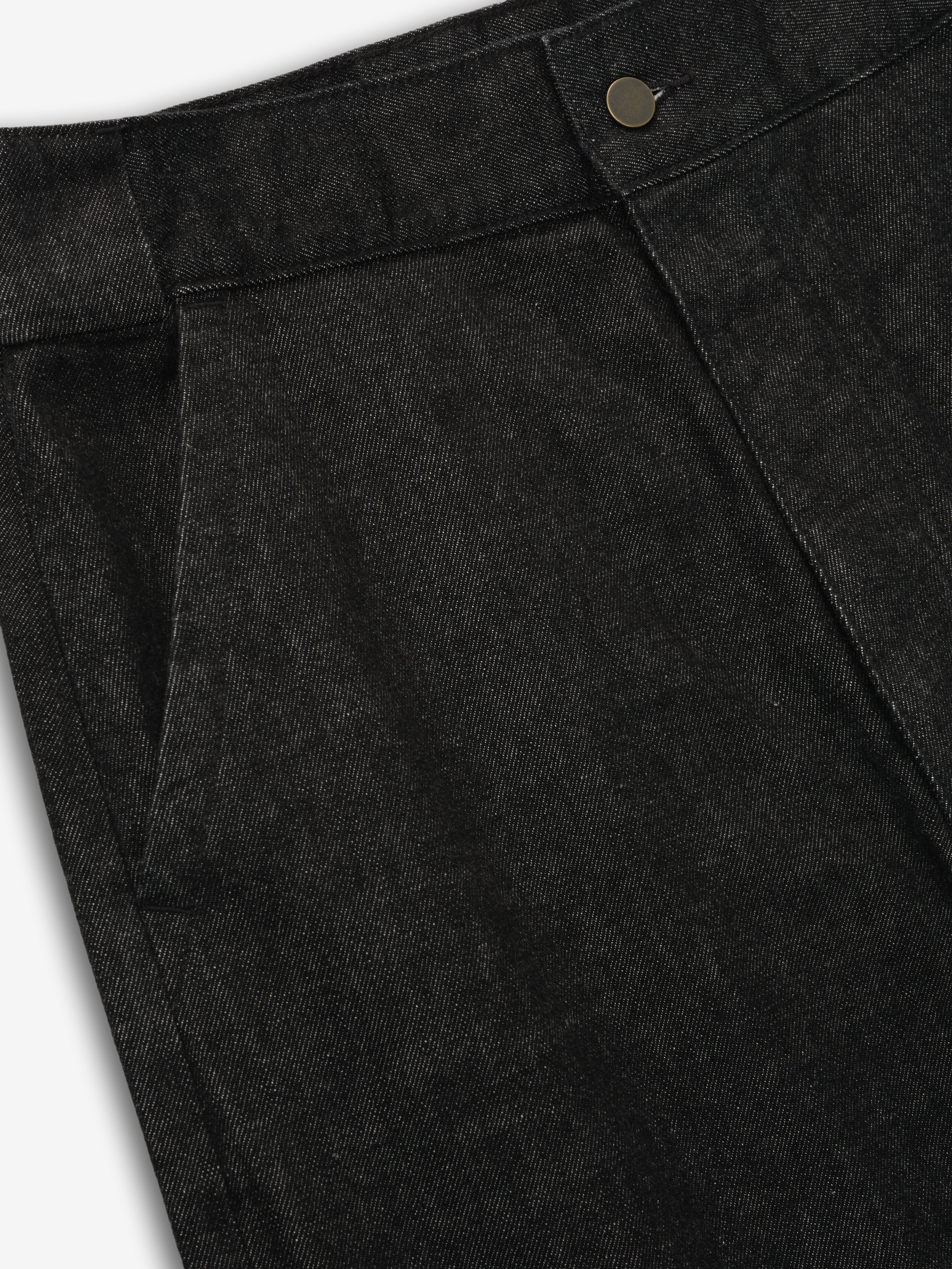 Close-up of vintage black denim work pant waistband and front pocket with button detail on gray background