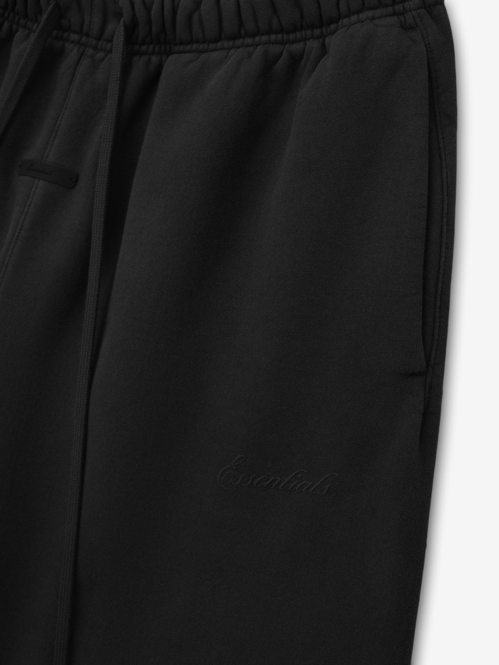 close-up of black heavyweight fleece sweatpants with elastic waistband, drawstring, side pockets, and tonal Essentials logo embroidery