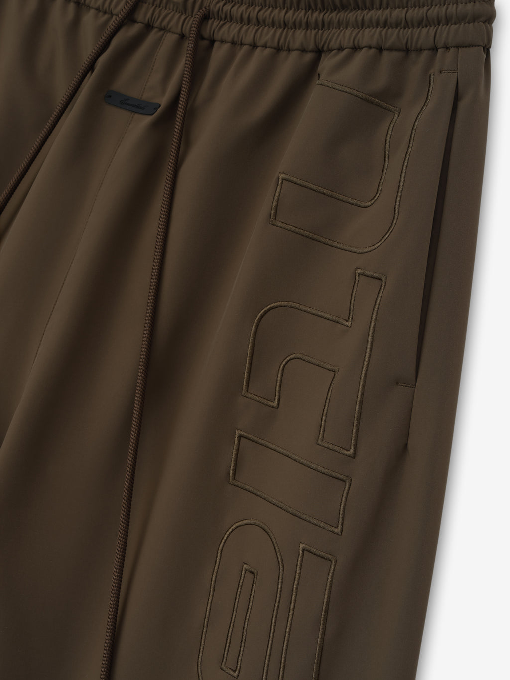 close-up of brown polyester women's track pants with elastic waistband and tonal stitched branding detail on leg