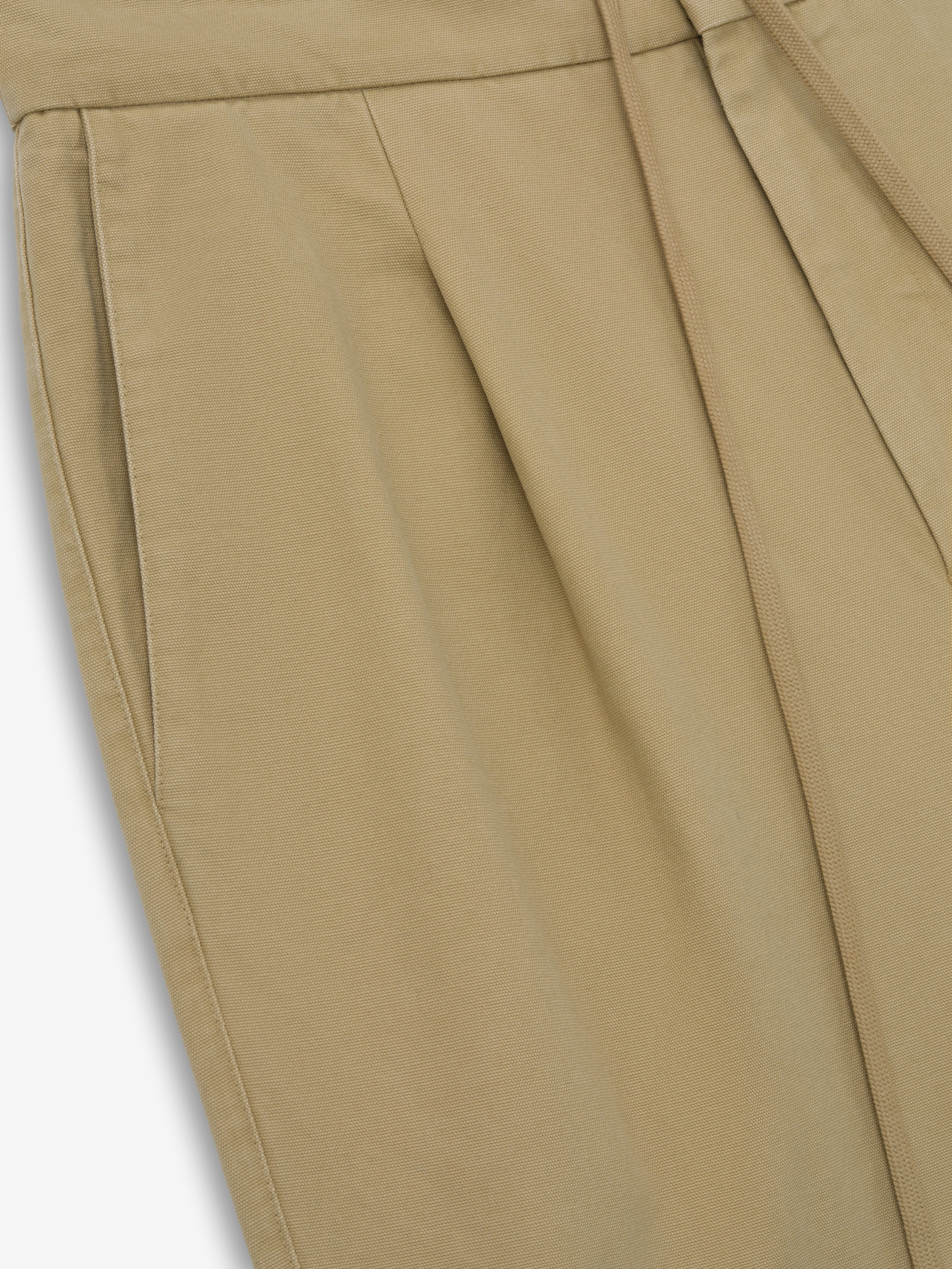 Close-up of beige tapered pants with side seam pocket and subtle front pleats on a light background