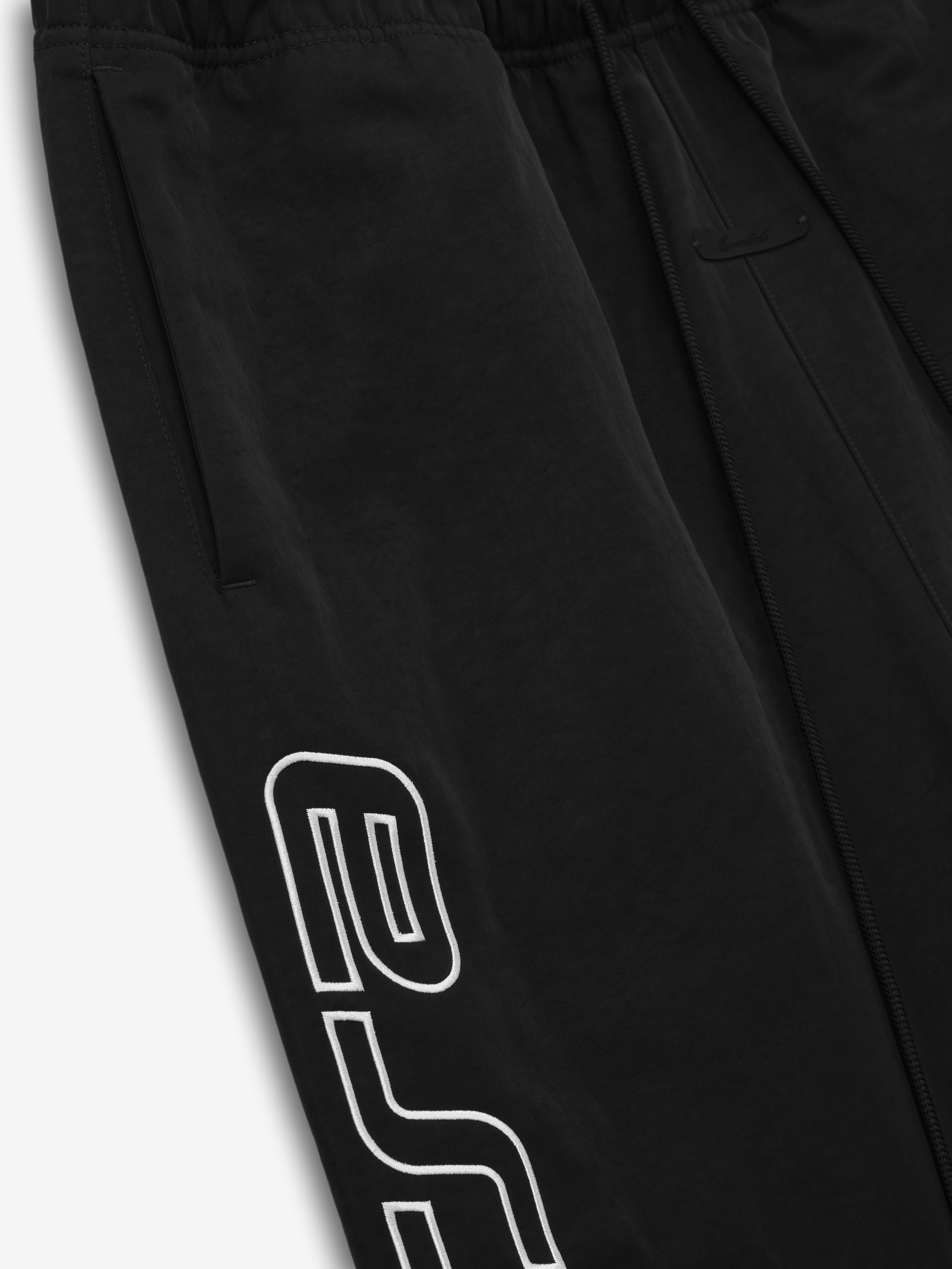 Close-up of black pants with side pocket and bold white outlined text detail on the side leg