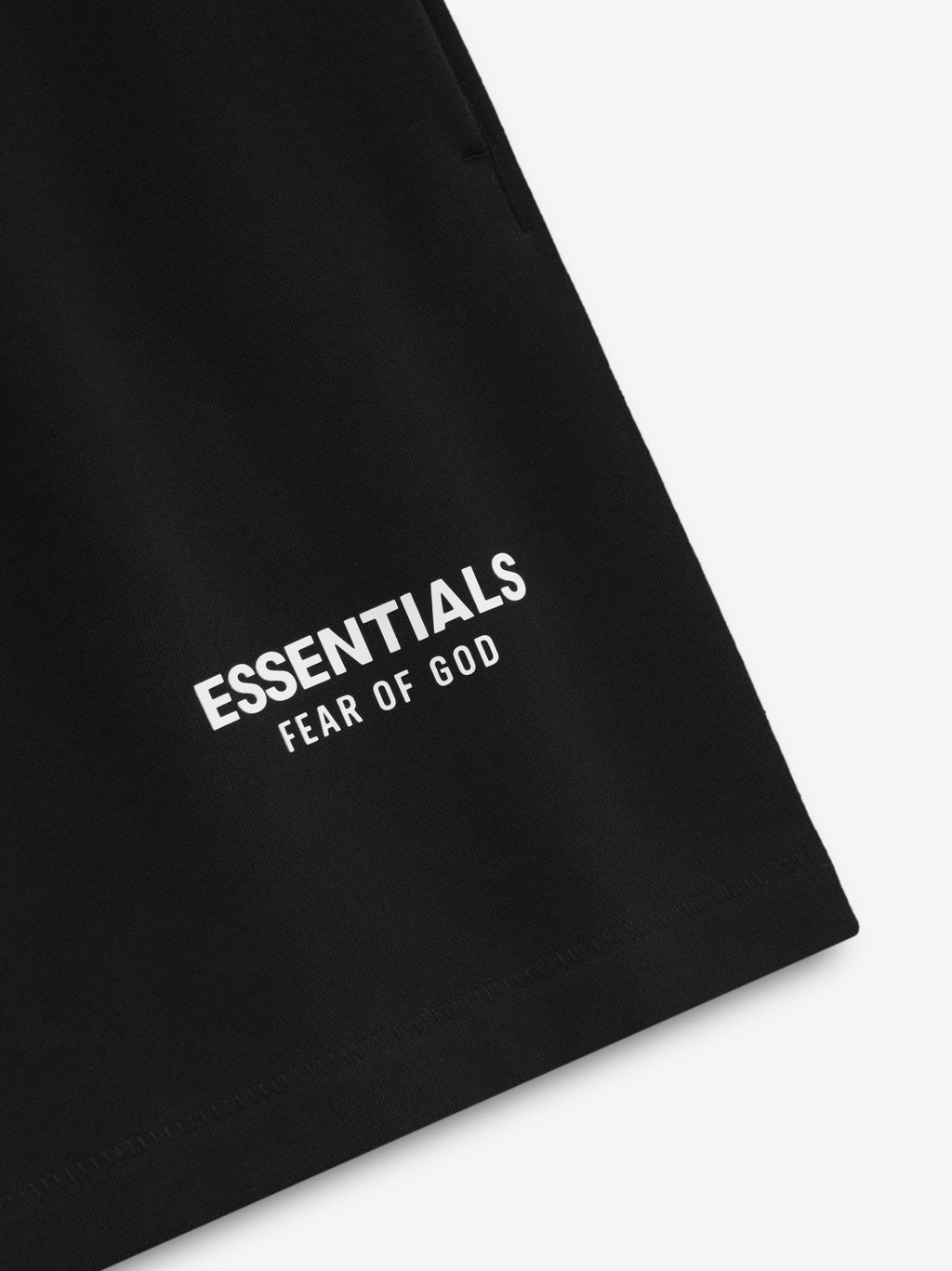 Close-up of jet black Classic Sweatshort showing white Essentials Fear of God logo near hem on smooth fabric