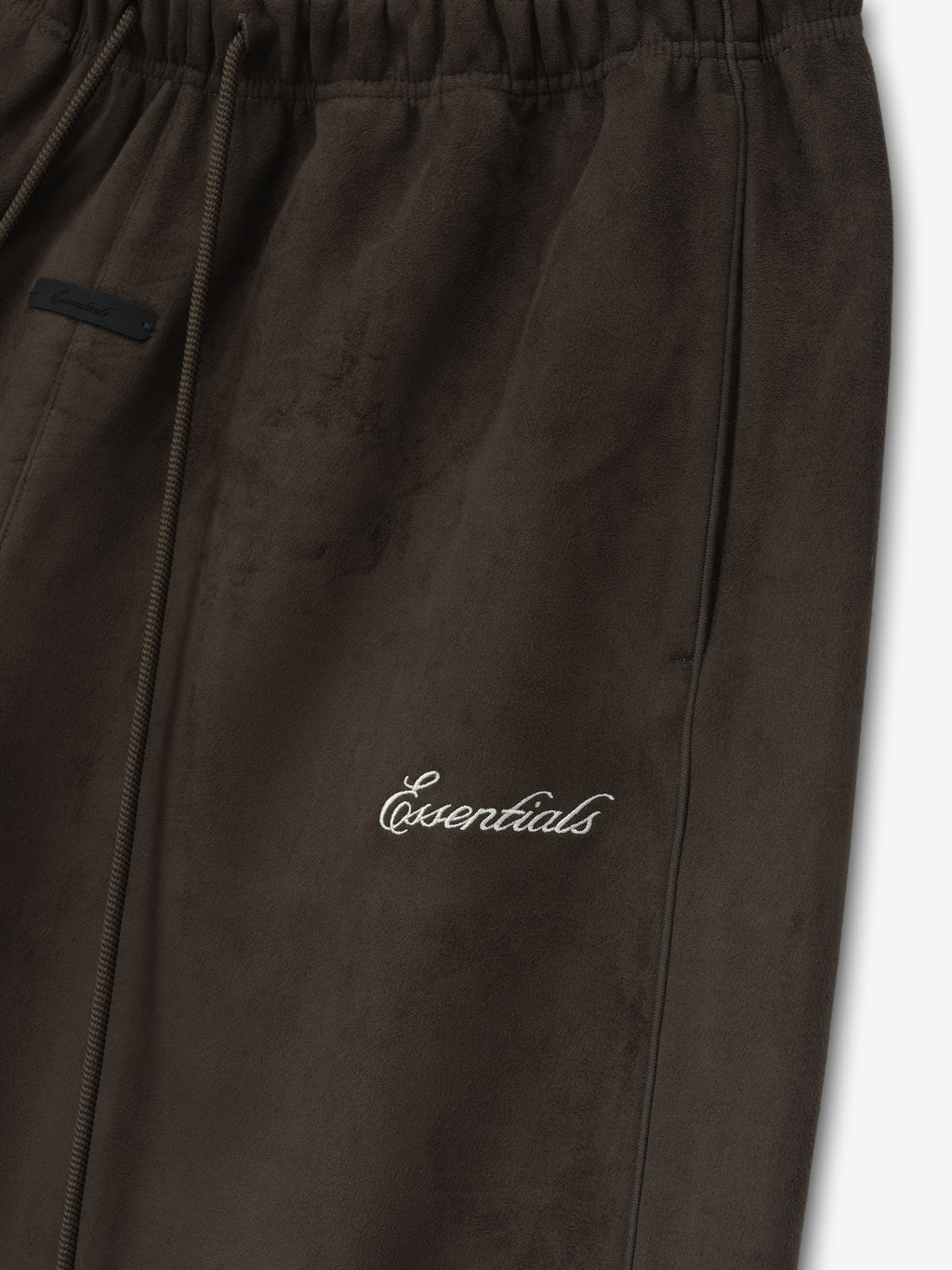 Close-up of dark brown pants with elastic waistband, side pocket, and white cursive "Essentials" embroidery on front leg