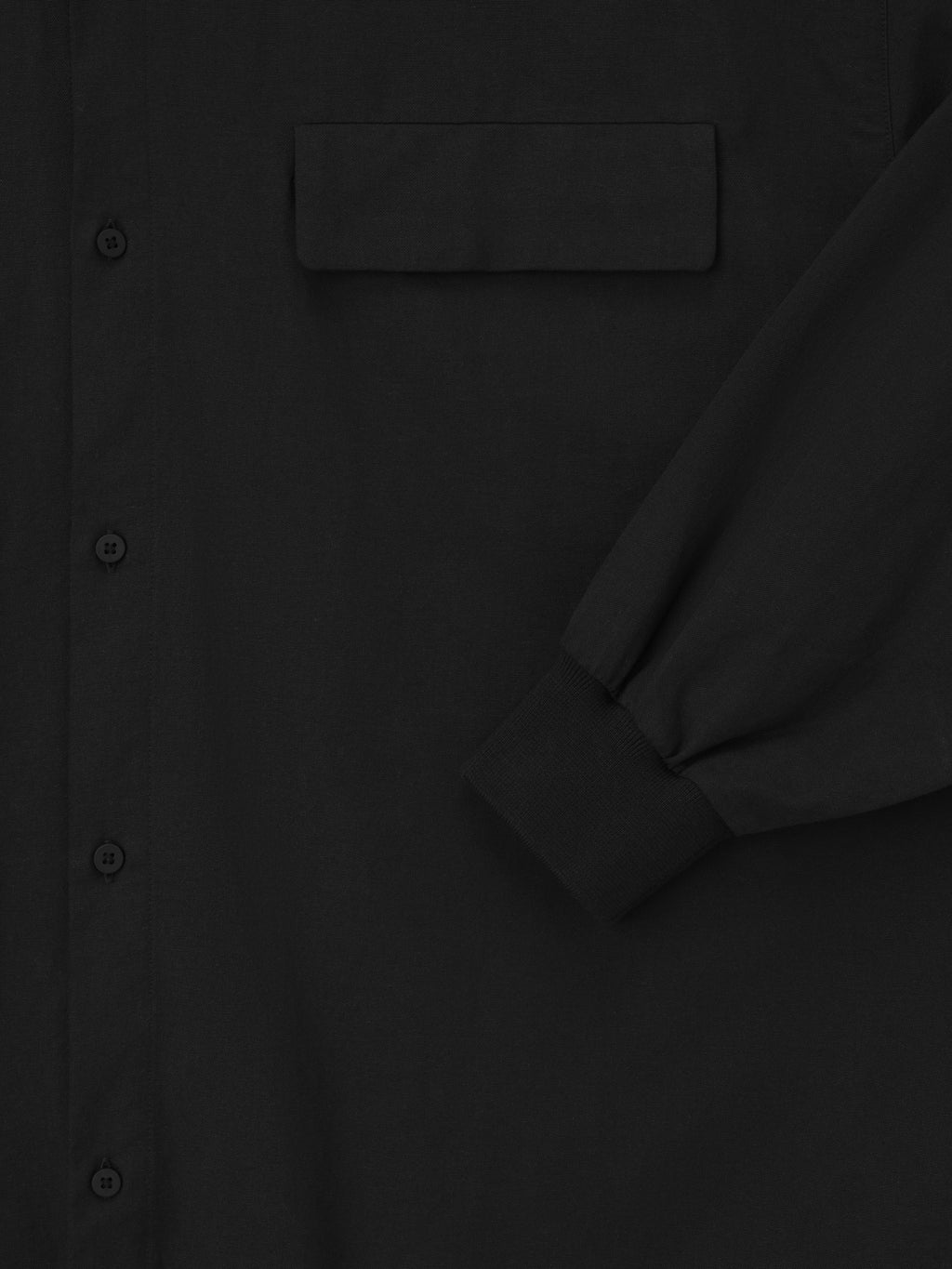 close-up of black Oxford shirt showing front buttons, flap chest pocket, and cuffed long sleeve detail