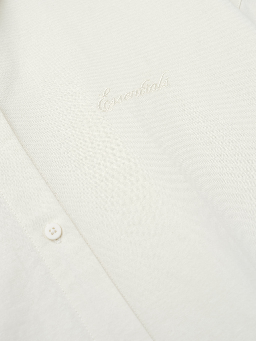 close-up of cream cotton oxford fabric with tonal Essentials embroidery and button detail on womens shirt