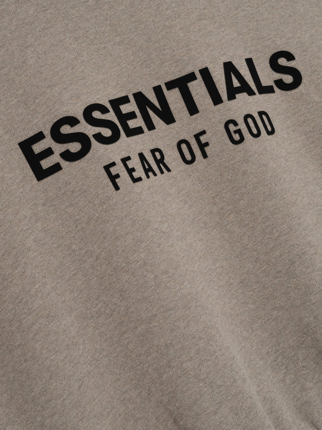 close-up of taupe heavyweight fleece fabric with black "ESSENTIALS FEAR OF GOD" logo printed on front