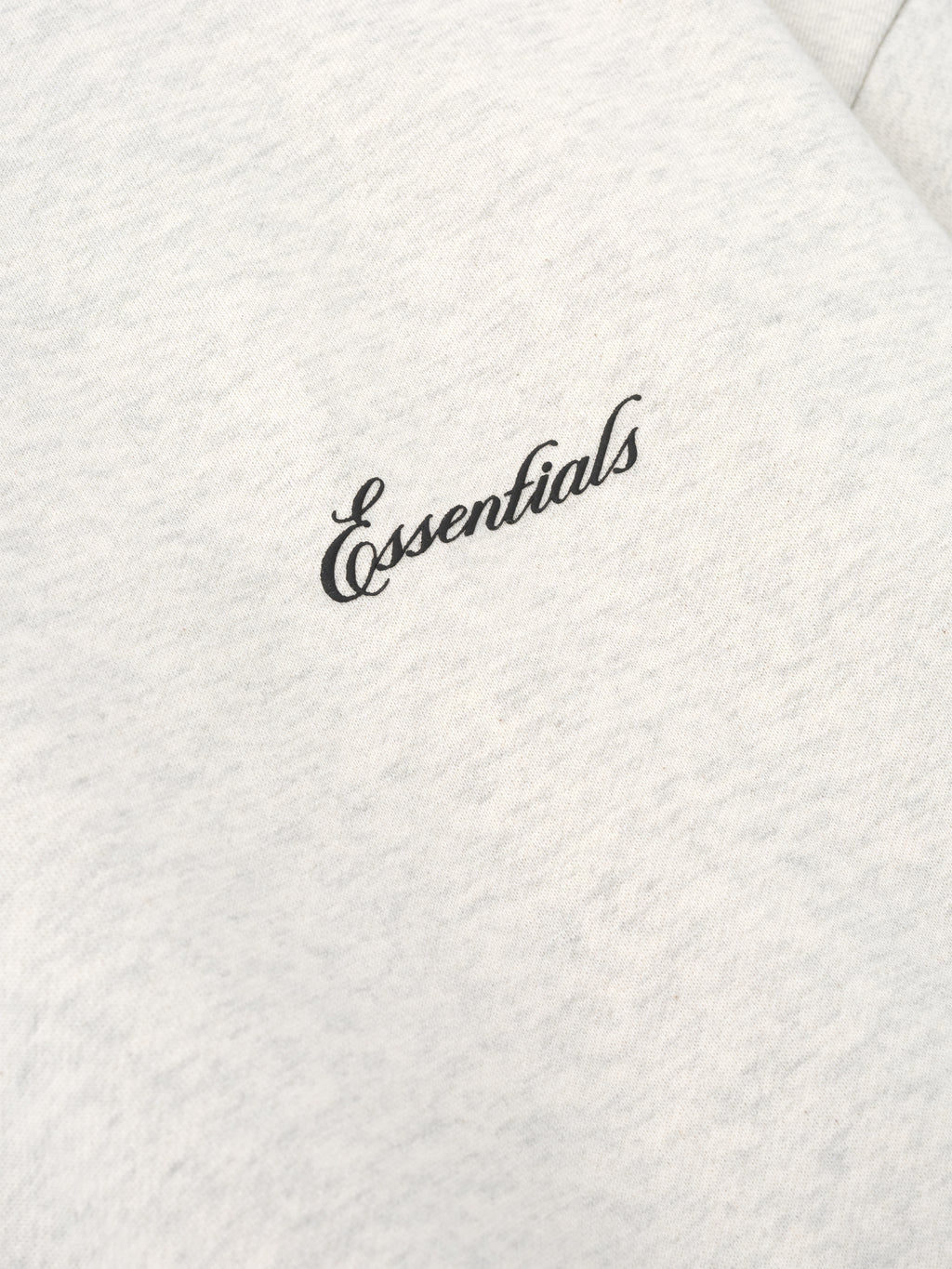 close-up of light cream crewneck sweatshirt fabric with black puff-printed Essentials logo on chest