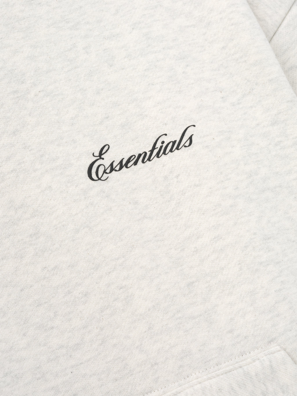 close-up of light heather grey fabric with black puff-printed Essentials signature logo on chest area of hoodie