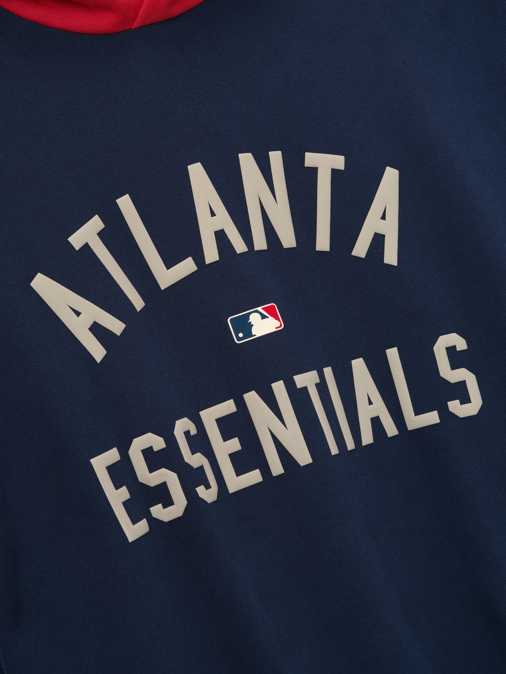 Close-up of navy hoodie featuring beige "ATLANTA ESSENTIALS" text with small MLB logo centered on front panel