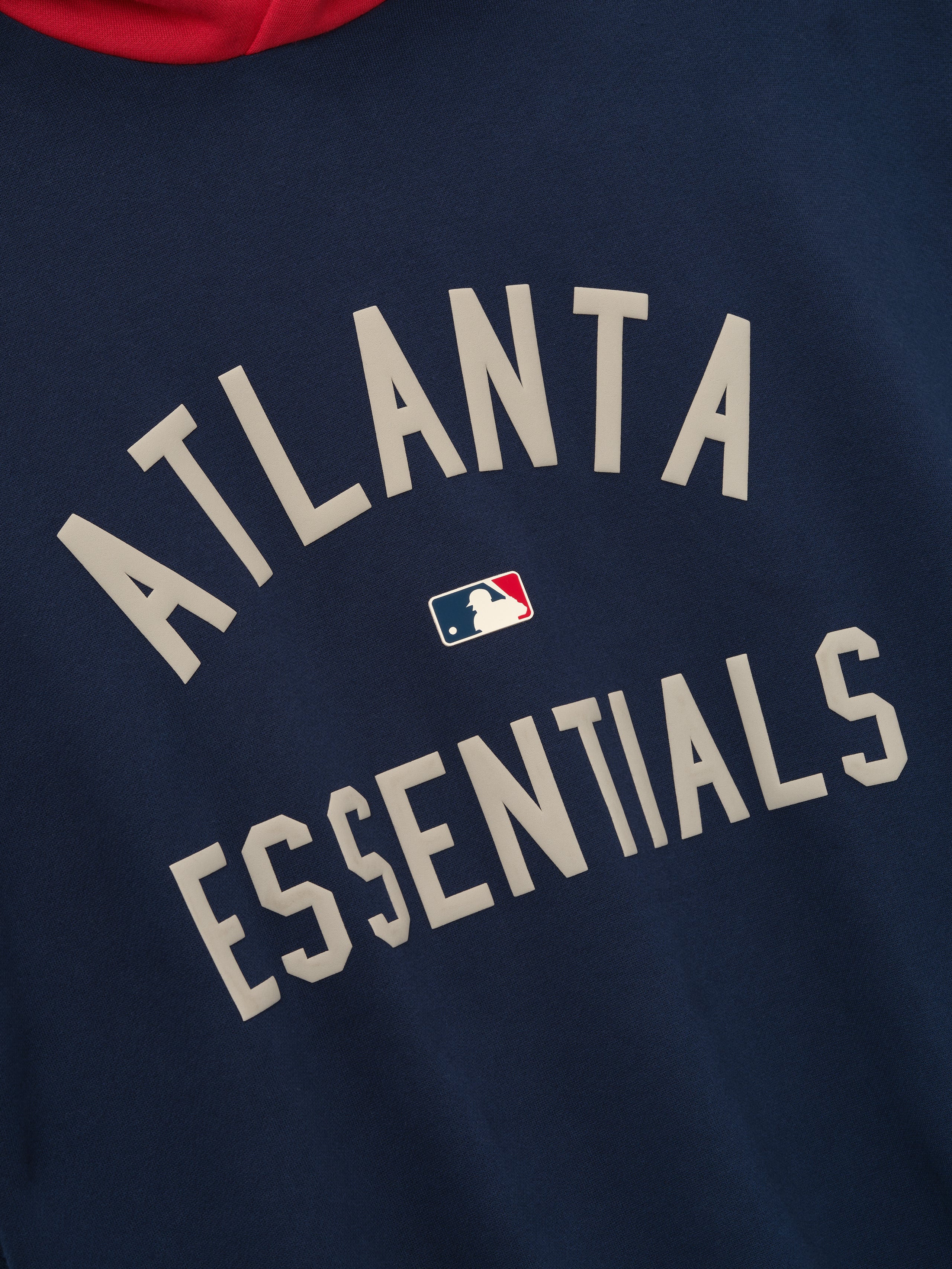 Close-up of navy hoodie featuring beige "ATLANTA ESSENTIALS" text with small MLB logo centered on front panel