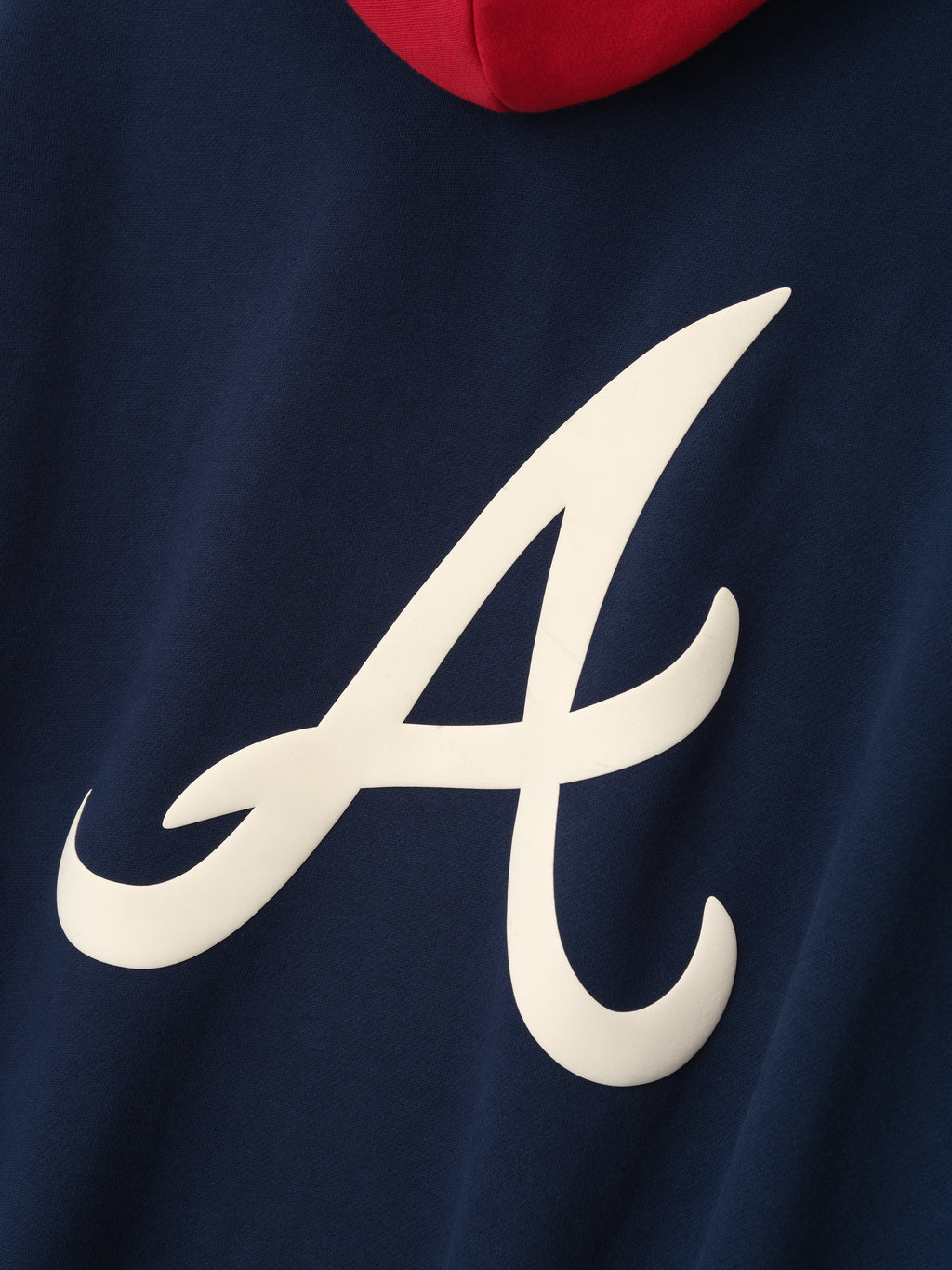 Close-up of navy hoodie showing large white stylized "A" logo with red hood detail on back panel