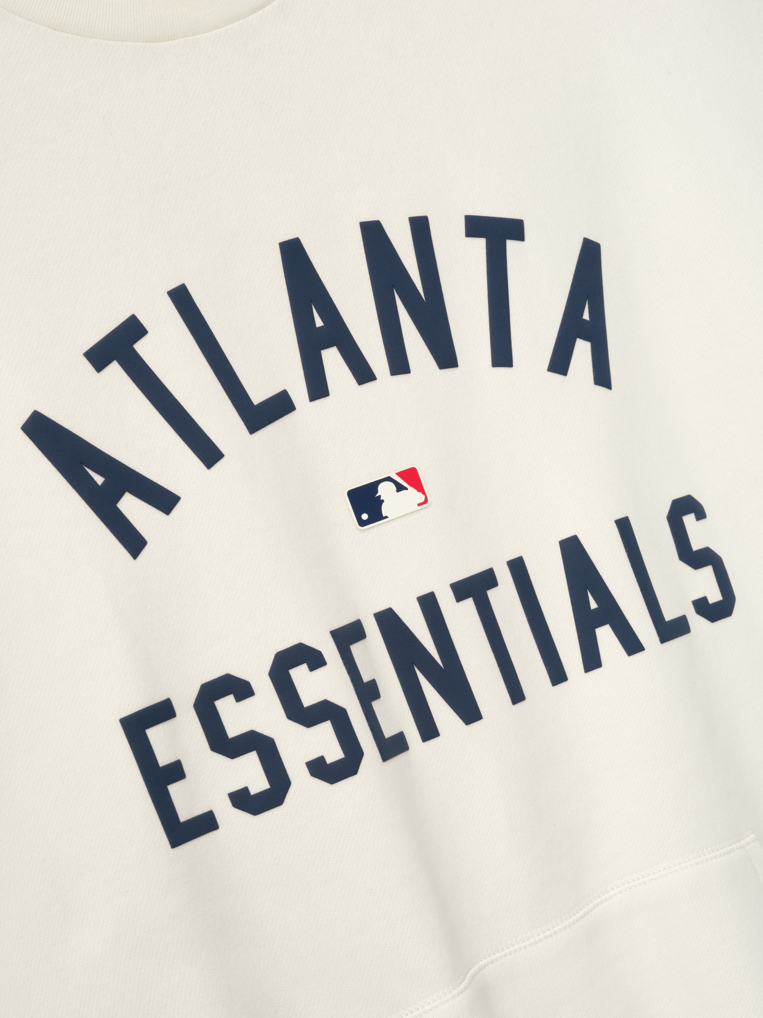 Off-white fabric close-up featuring navy blue "ATLANTA ESSENTIALS" text with small MLB logo centered between words