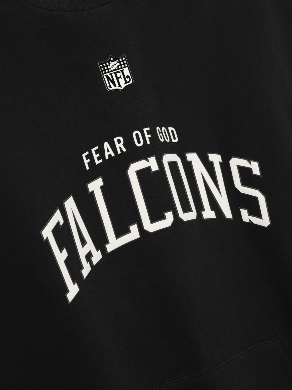 Black crewneck with white arched "FALCONS" text and small "FEAR OF GOD" above NFL logo on front fabric close-up