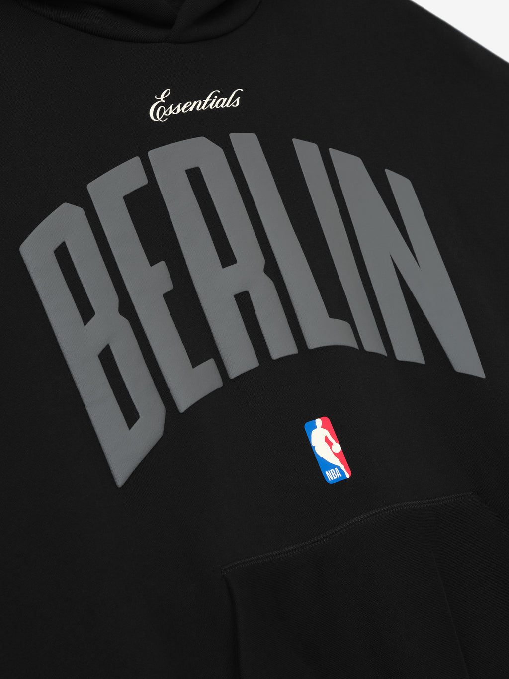 Black Berlin 90's Hoodie close-up showing curved grey Berlin text, white Essentials script, and NBA logo above front pocket, gallery 0