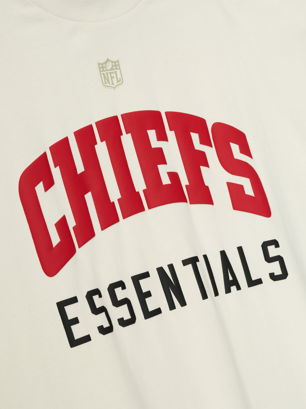 Close-up of cream white Chiefs 90s 3/4 Sleeve Football Tee showing red Chiefs text and black Essentials below center chest with subtle NFL shield above