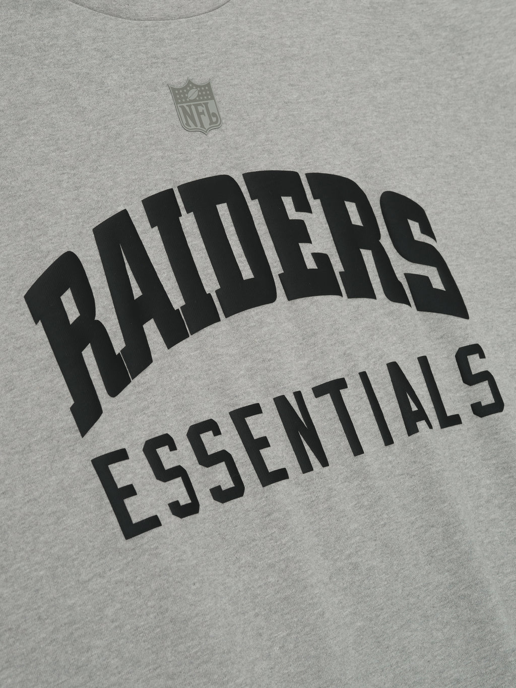 Close-up of concrete heather Raiders 90s 3/4 Sleeve Football Tee showing black Raiders Essentials text and NFL logo above