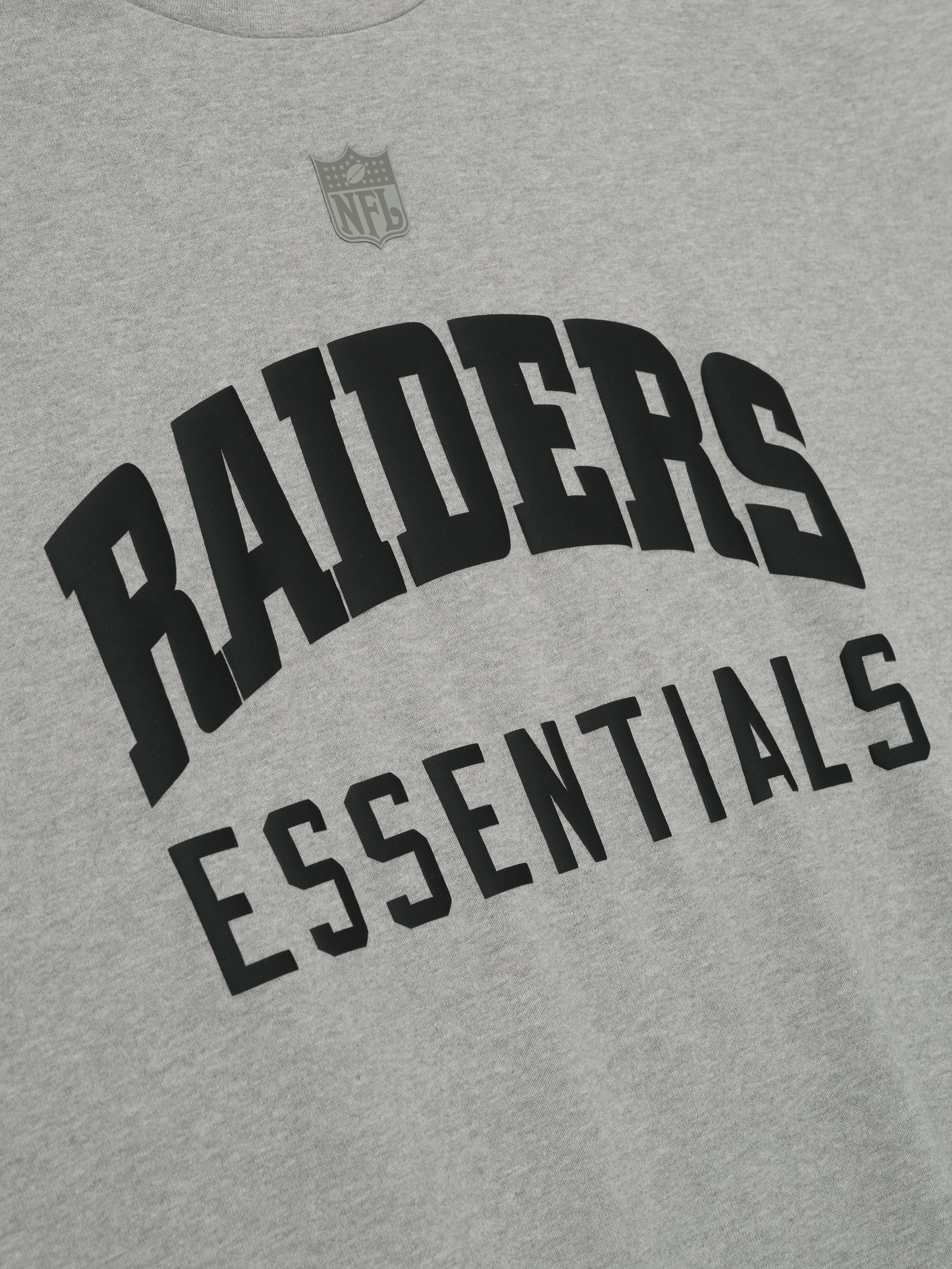 Close-up of concrete heather Raiders 90s 3/4 Sleeve Football Tee showing black Raiders Essentials text and NFL logo above