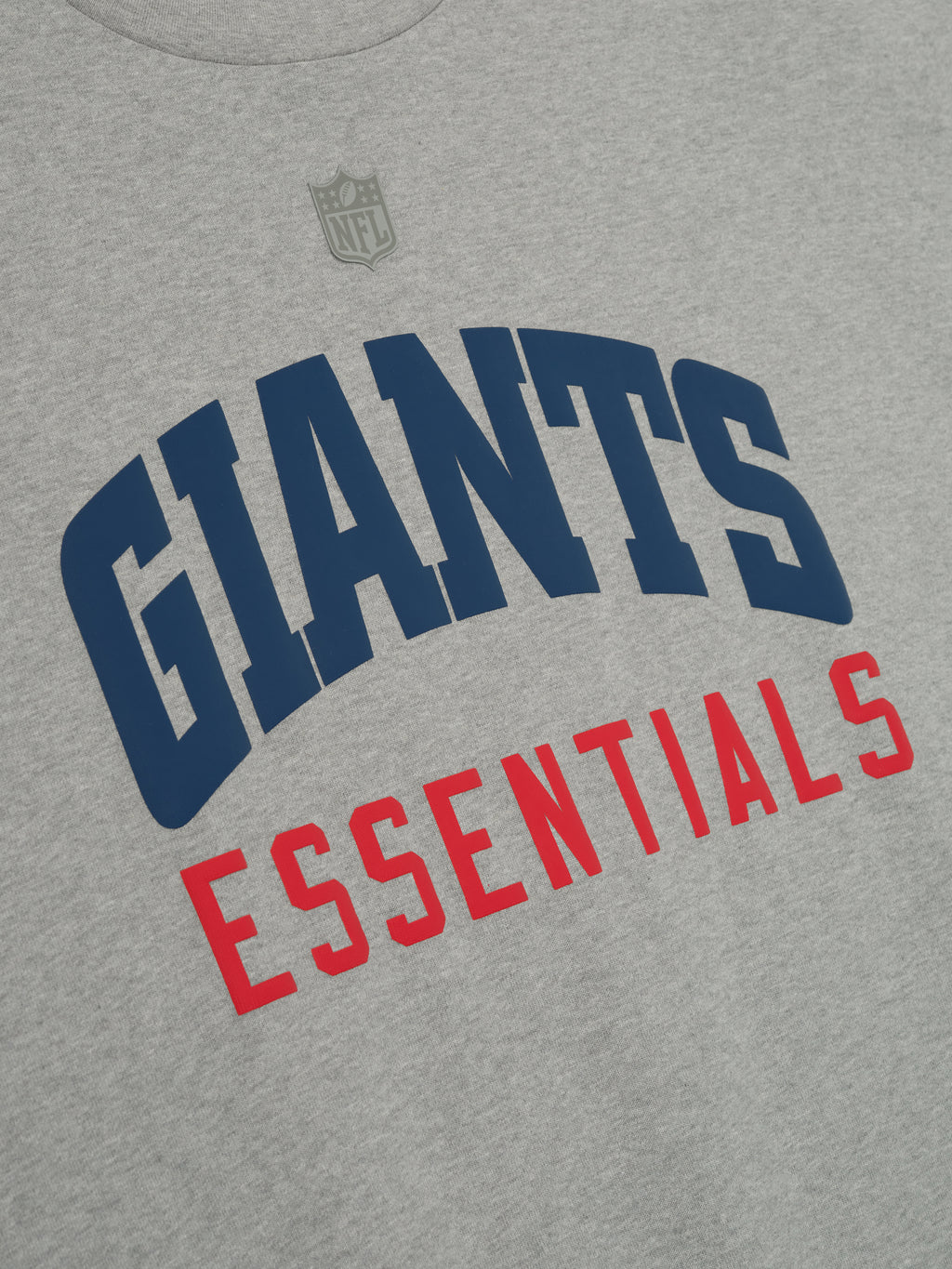 Close-up of concrete heather Giants 90s 3/4 Sleeve Football Tee showing navy Giants and red Essentials text on chest