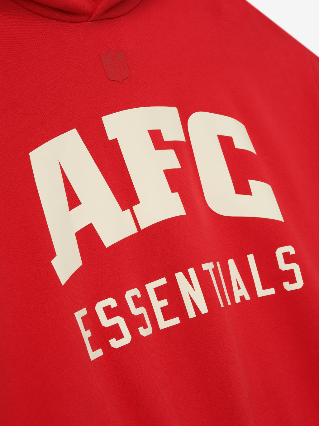 Close-up of red American Sport Hoodie showing large cream AFC Essentials text with a subtle embossed NFL shield above