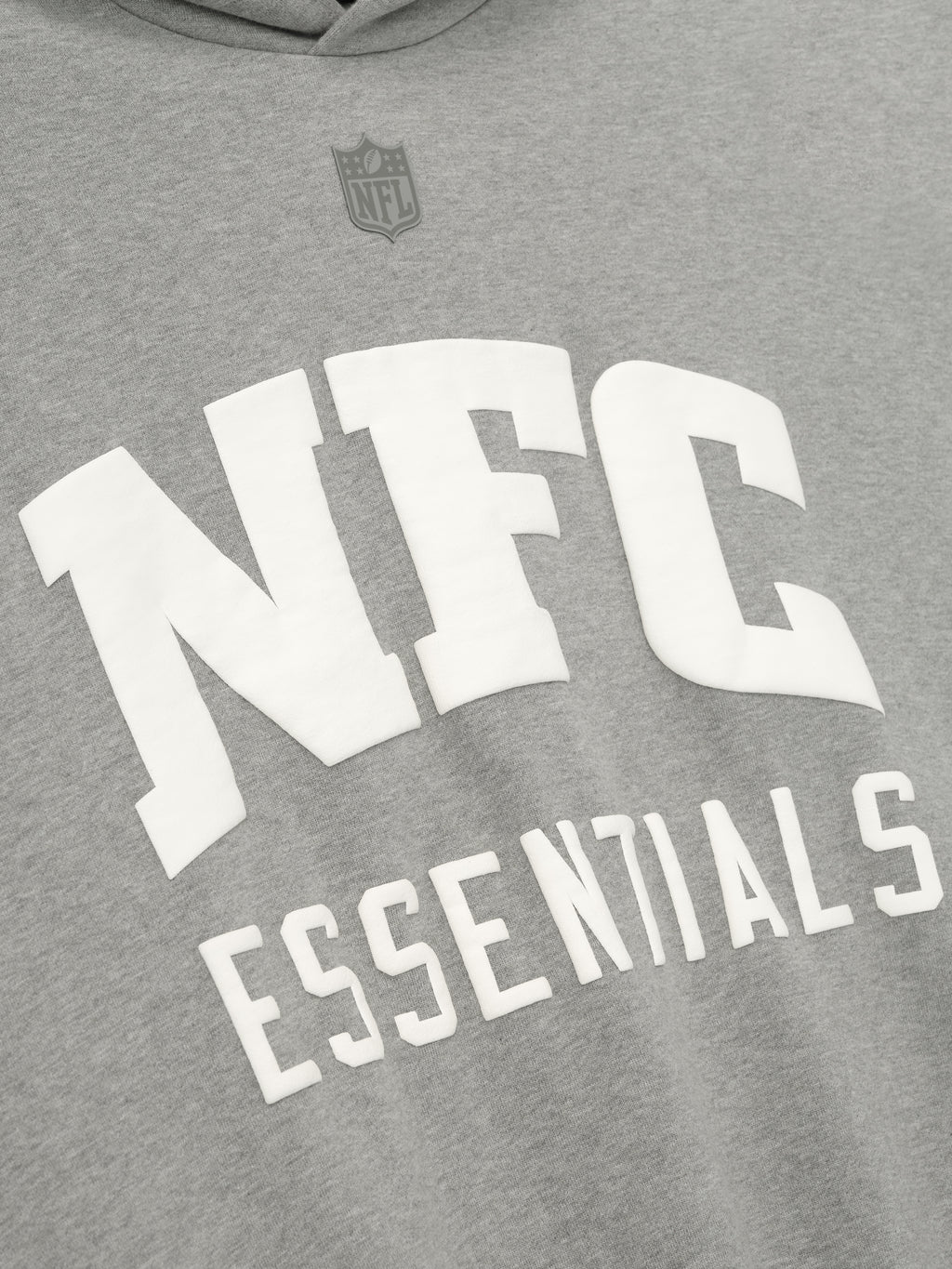 Close-up of concrete heather National Sport Hoodie showing white NFC Essentials text and subtle NFL shield above the chest