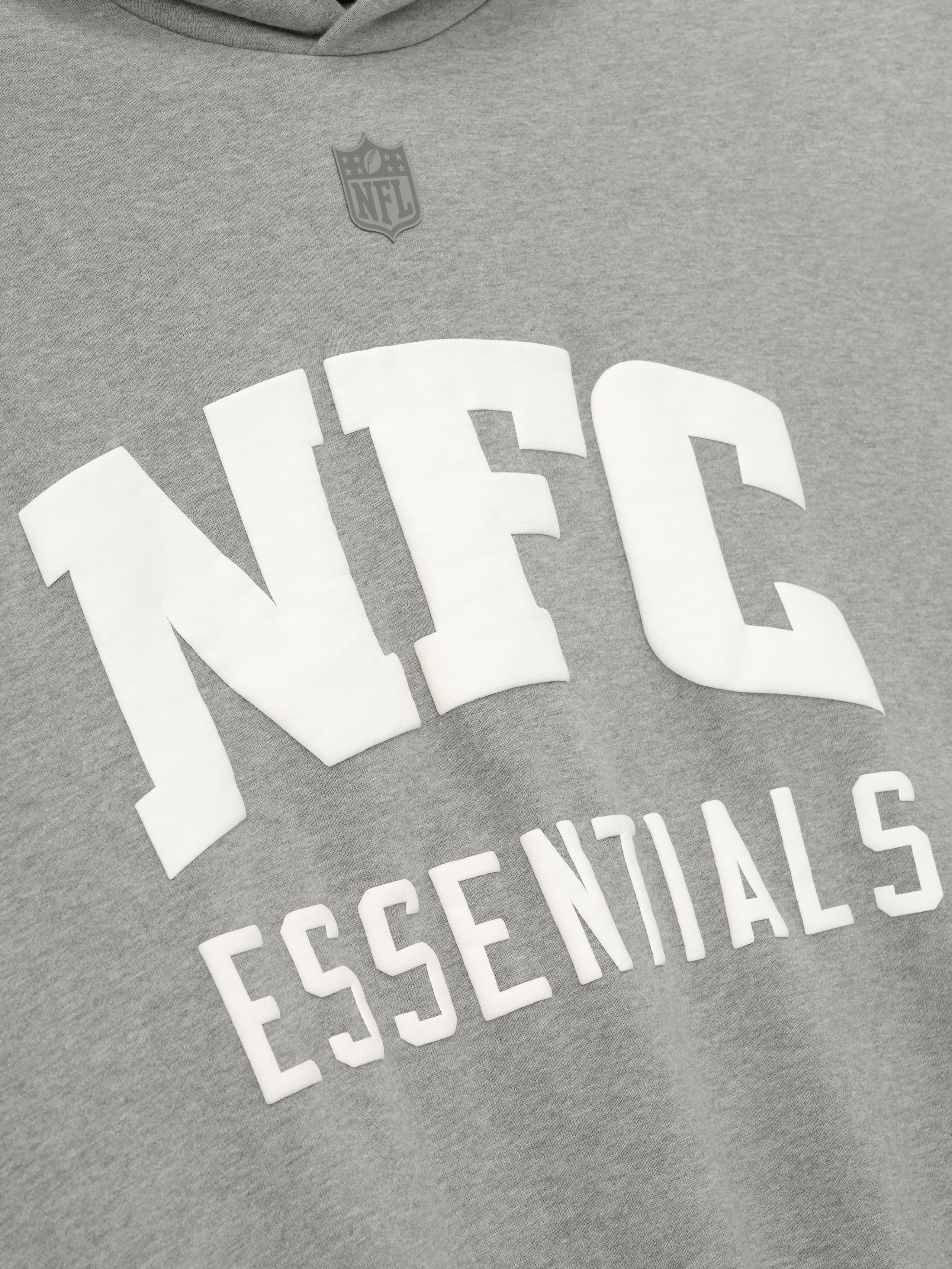 Close-up of concrete heather National Sport Hoodie showing white NFC Essentials text and subtle NFL shield above the chest