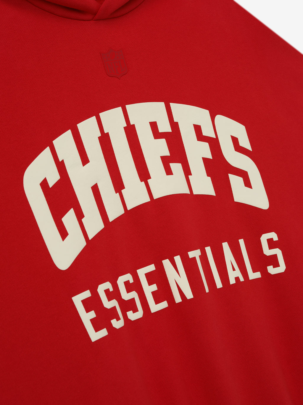 Close-up of red Chiefs Sport Hoodie showing cream Essentials text with subtle embossed NFL shield above the chest