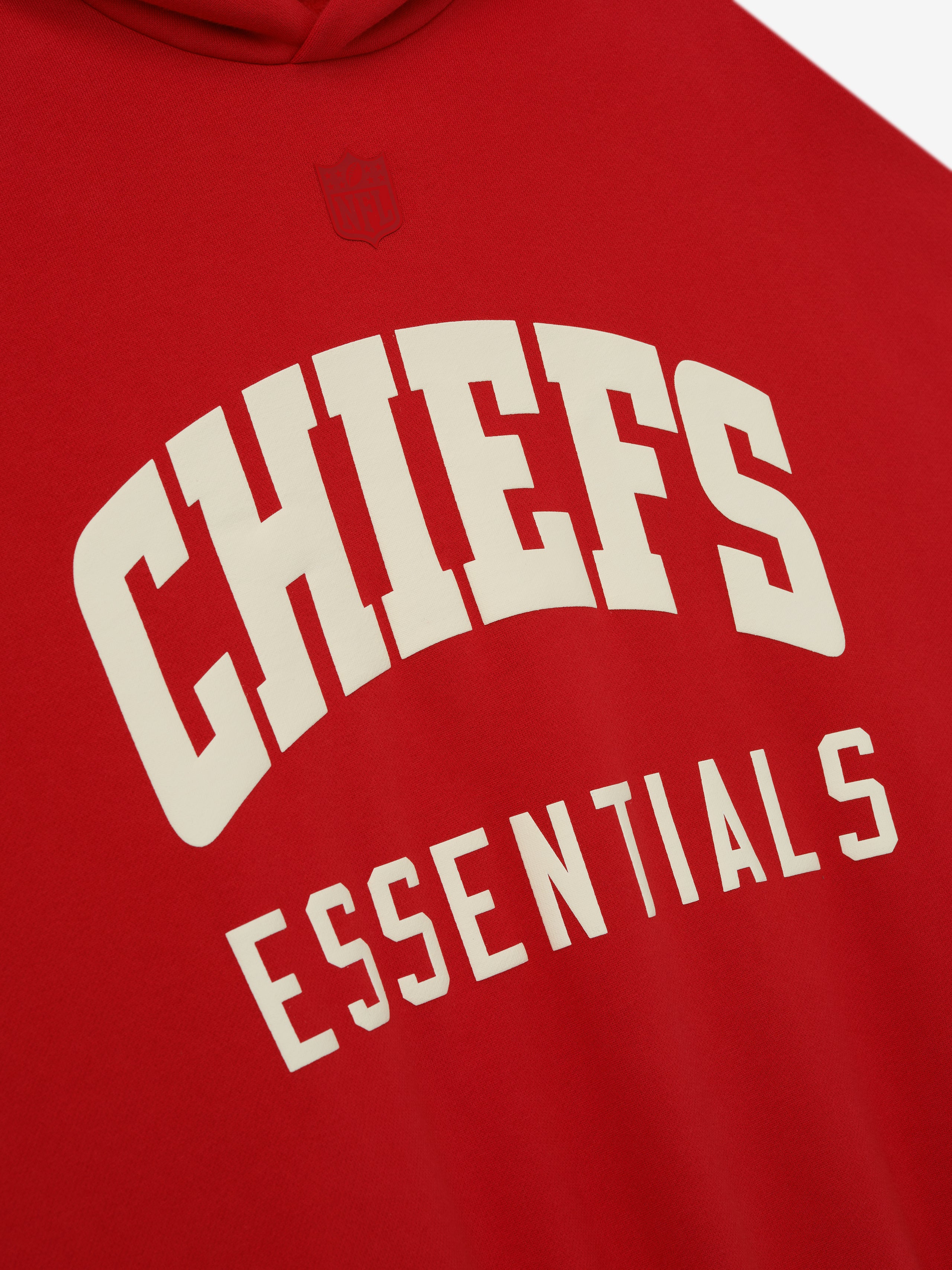Close-up of red Chiefs Sport Hoodie showing cream Essentials text with subtle embossed NFL shield above the chest